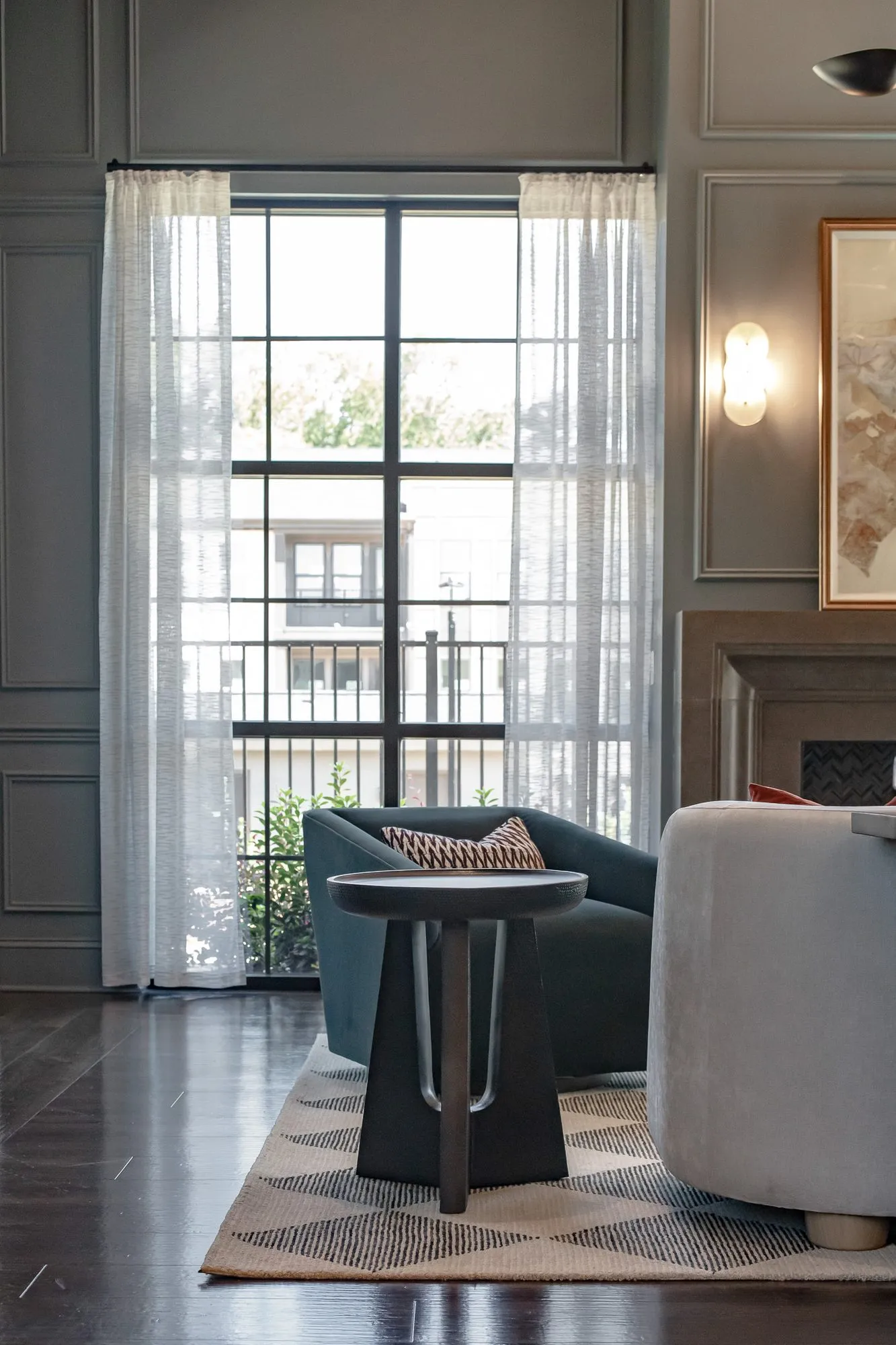 Multifamily amenity lounge with a dark teal swivel chair and grey boucle chair by a tall window with sheers