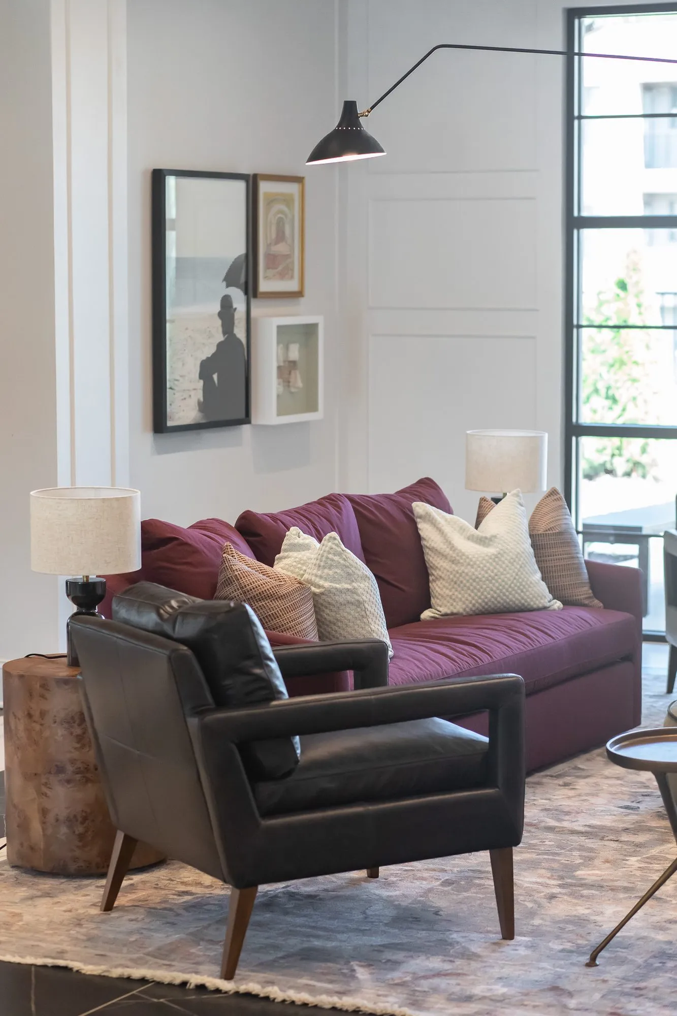 Multifamily amenity clubroom with a burgundy sofa and black leather armchair on a patterned rug by a tall window
