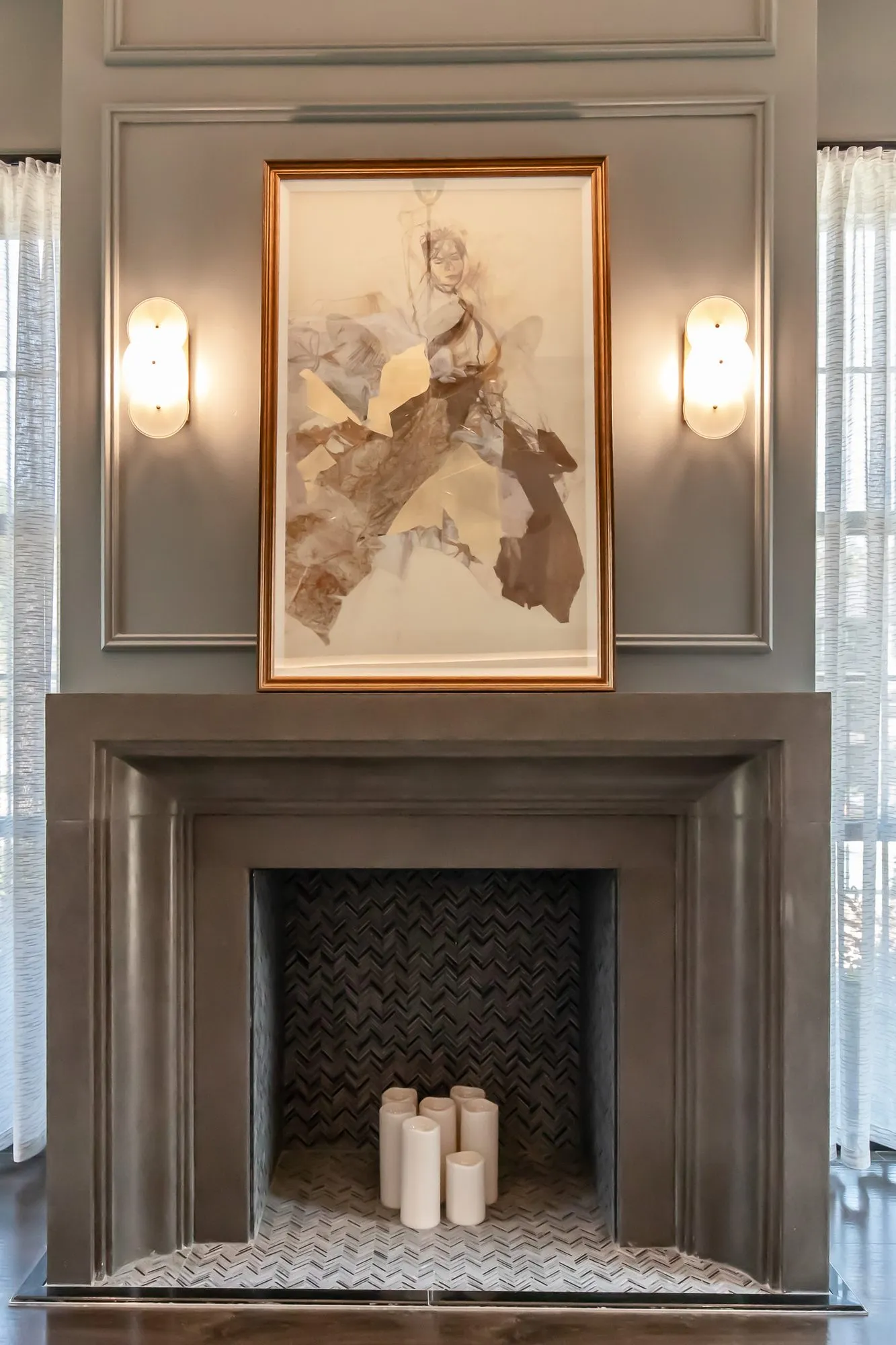 Multifamily amenity sitting room fireplace of dark stone with pillar candles below a framed abstract collage between sconces