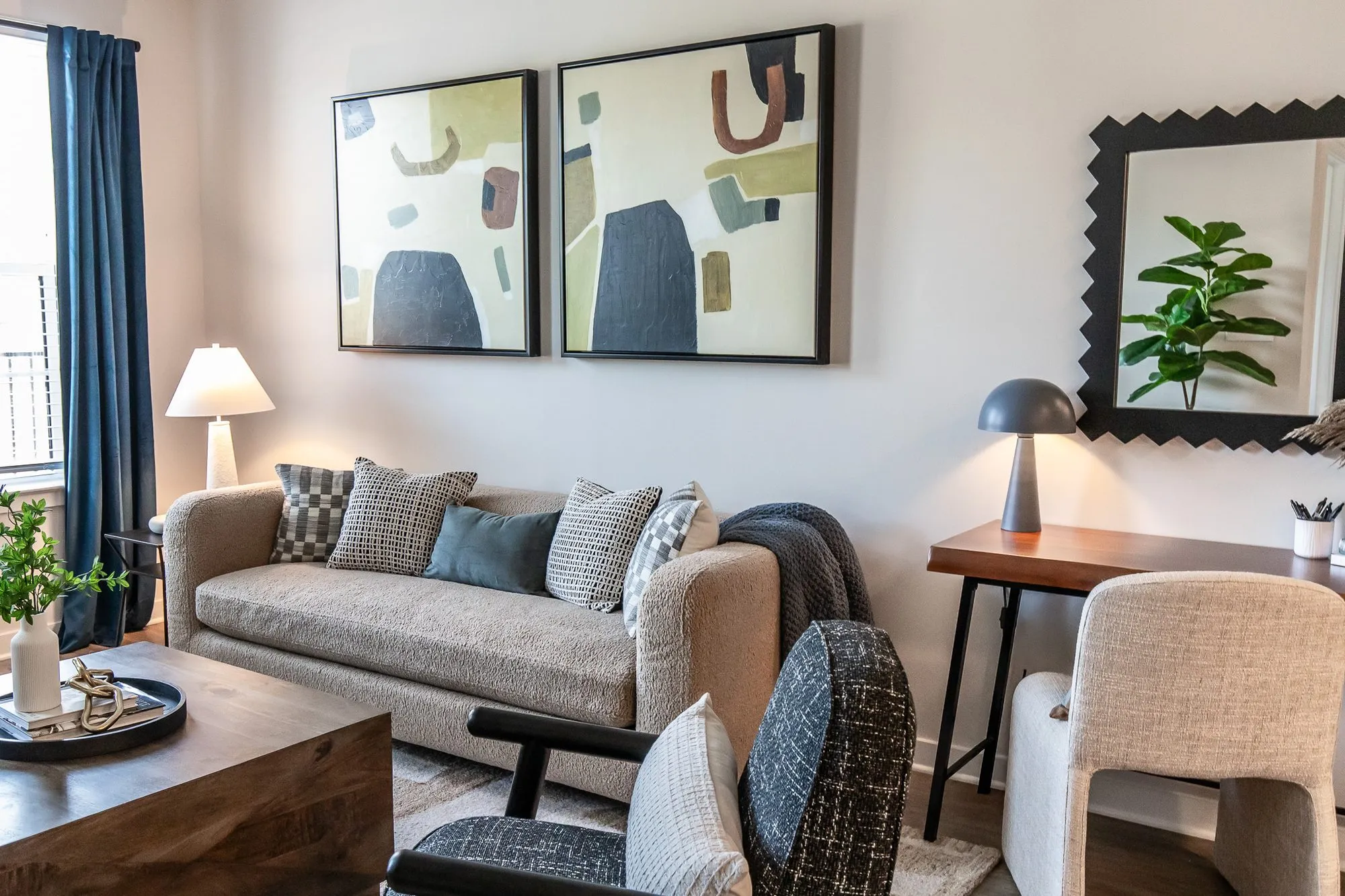 Multifamily apartment model living room seen past a black patterned armchair, a taupe sofa below abstract prints and a desk