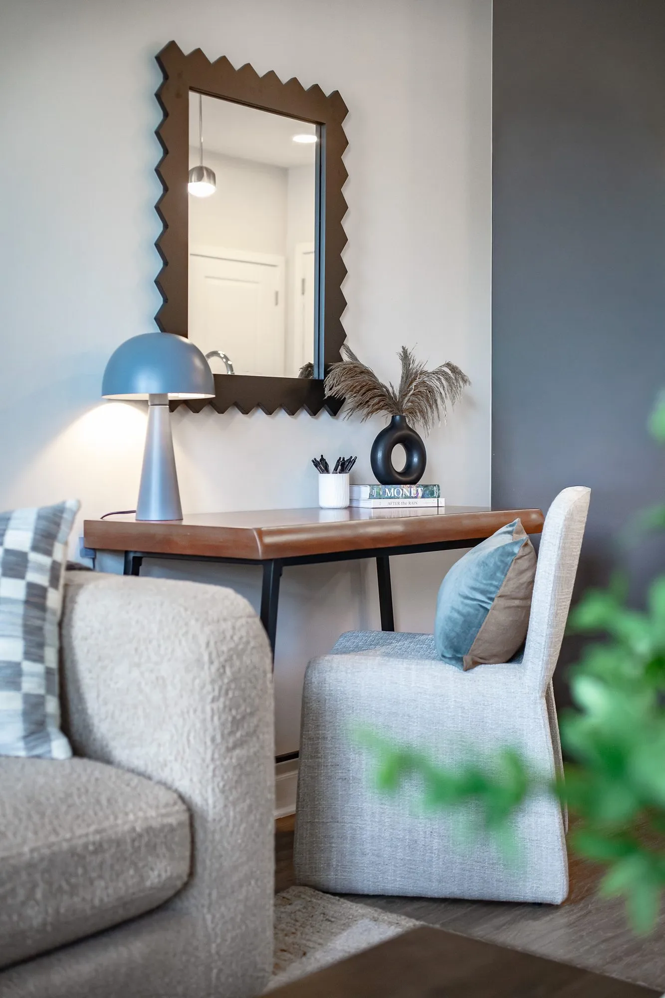 Multifamily apartment model living room desk with a mushroom lamp below a zigzag framed mirror, boucle chairs in front