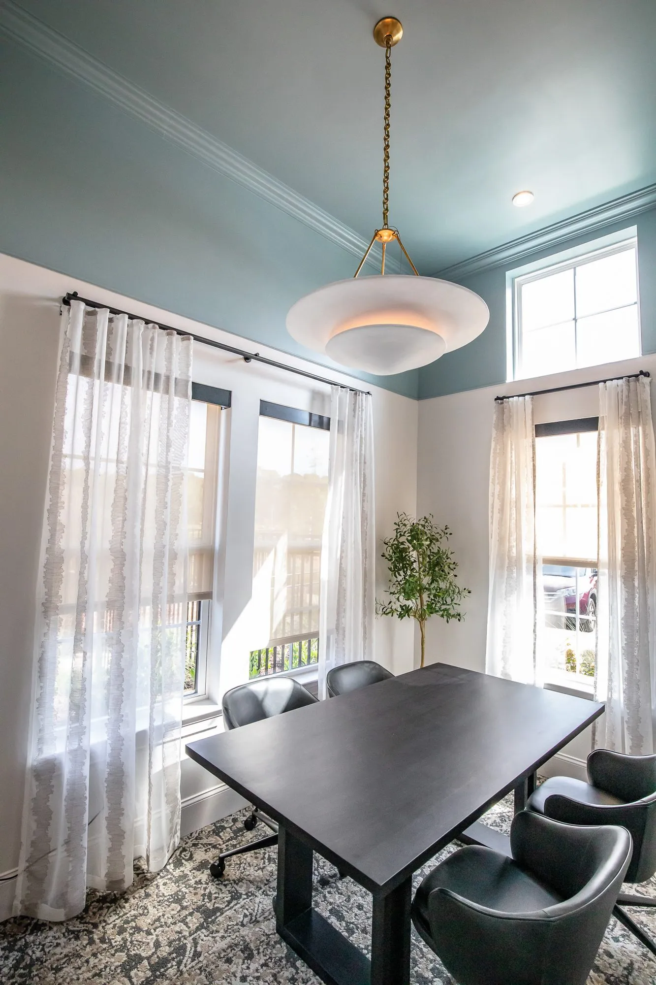 Multifamily amenity conference room with black leather chairs at a dark table under an alabaster pendant and a teal ceiling