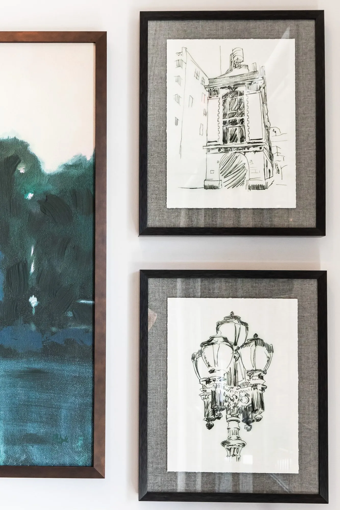 Multifamily interior detail: two framed black ink sketches of a building and a street lamp beside a dark green abstract