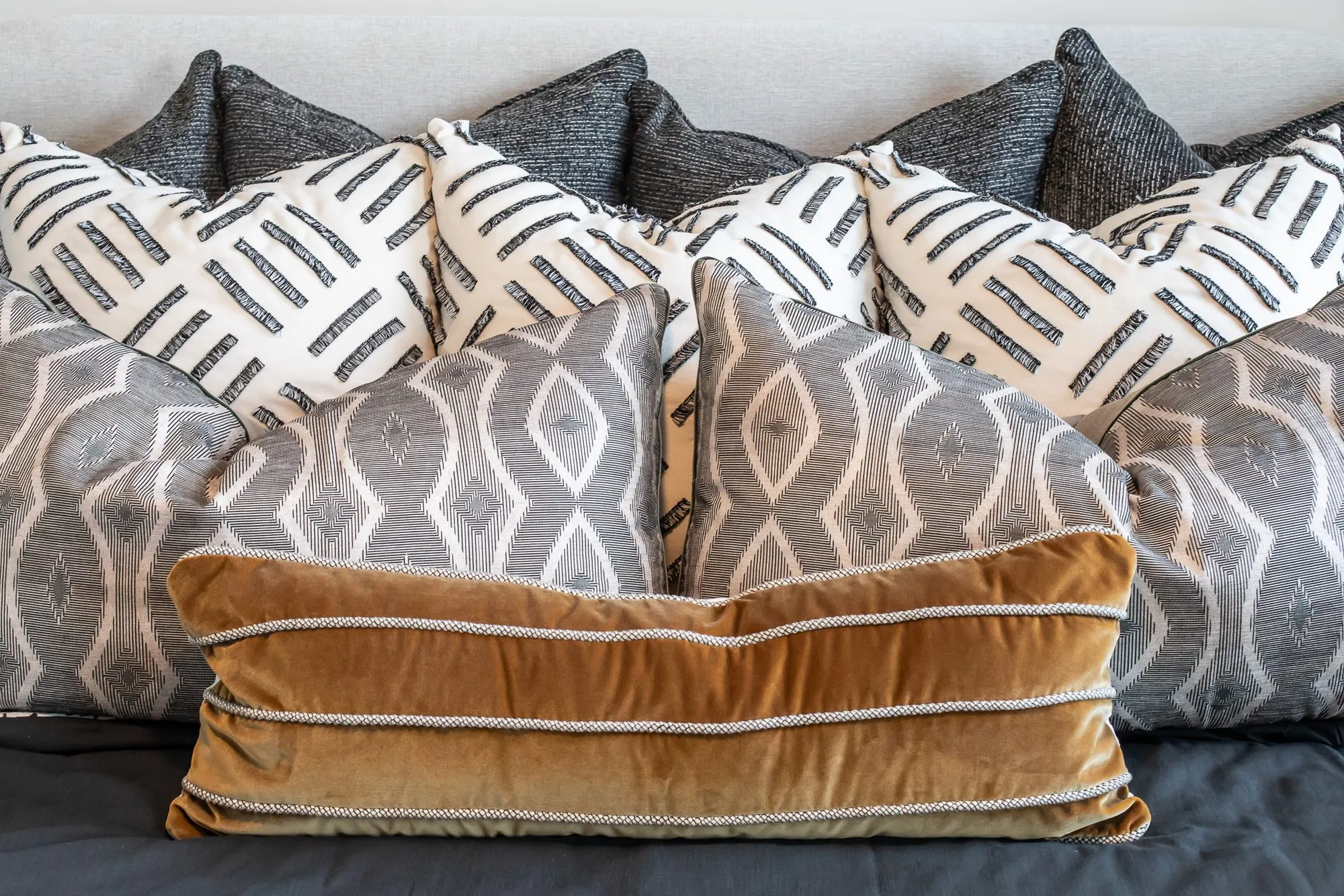 Multifamily apartment interior detail: bed of grey, white and black patterned pillows with a bronze velvet lumbar cushion