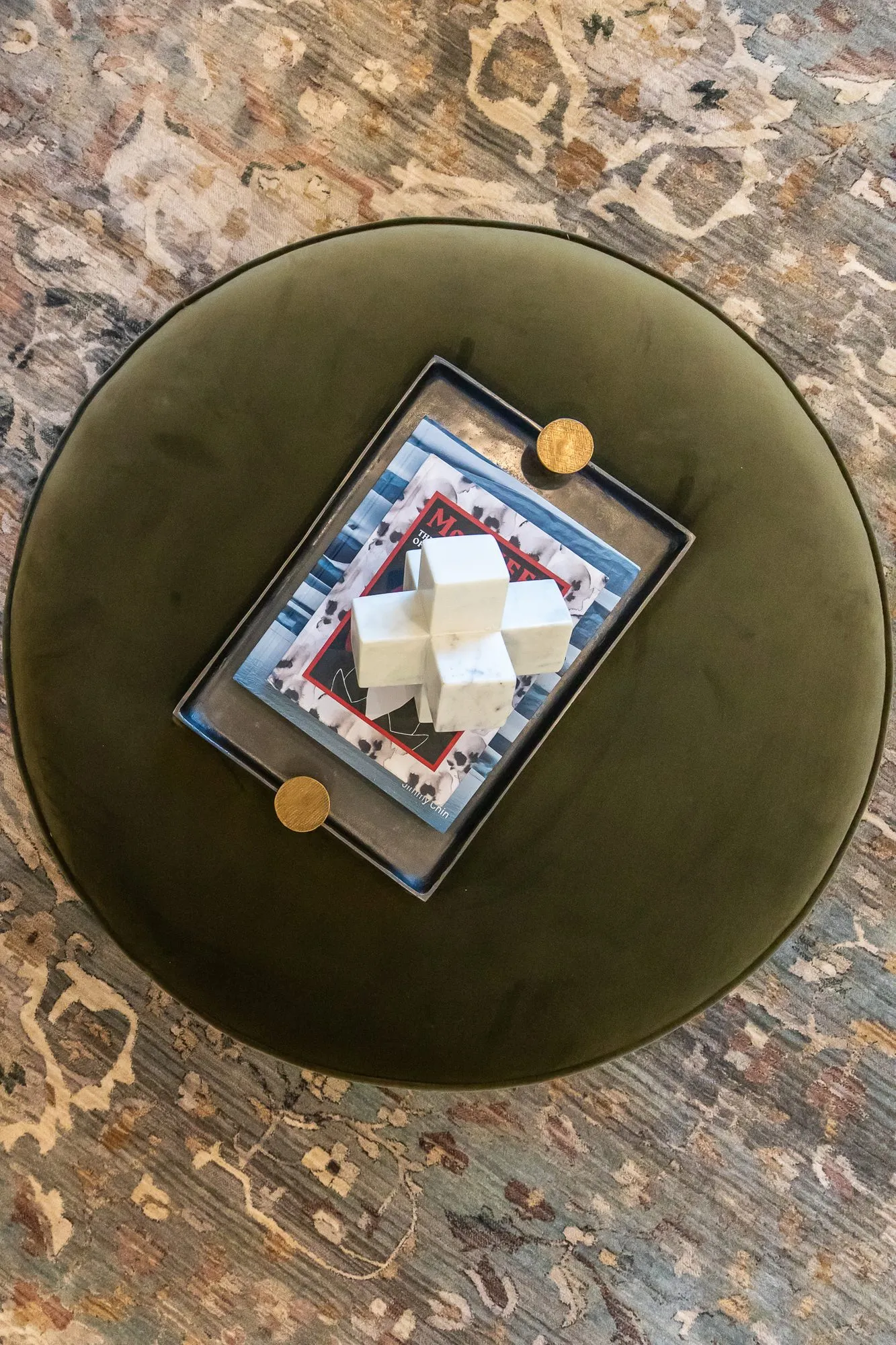 Multifamily amenity clubroom from above, a round olive velvet ottoman with a tray holding a white sculpture