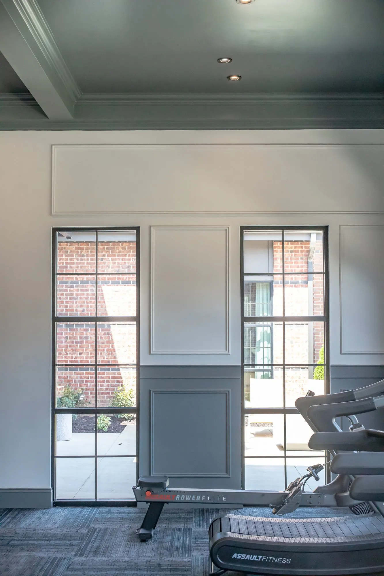 Multifamily amenity fitness room with treadmills by black framed windows, grey panelling and a dark coffered ceiling
