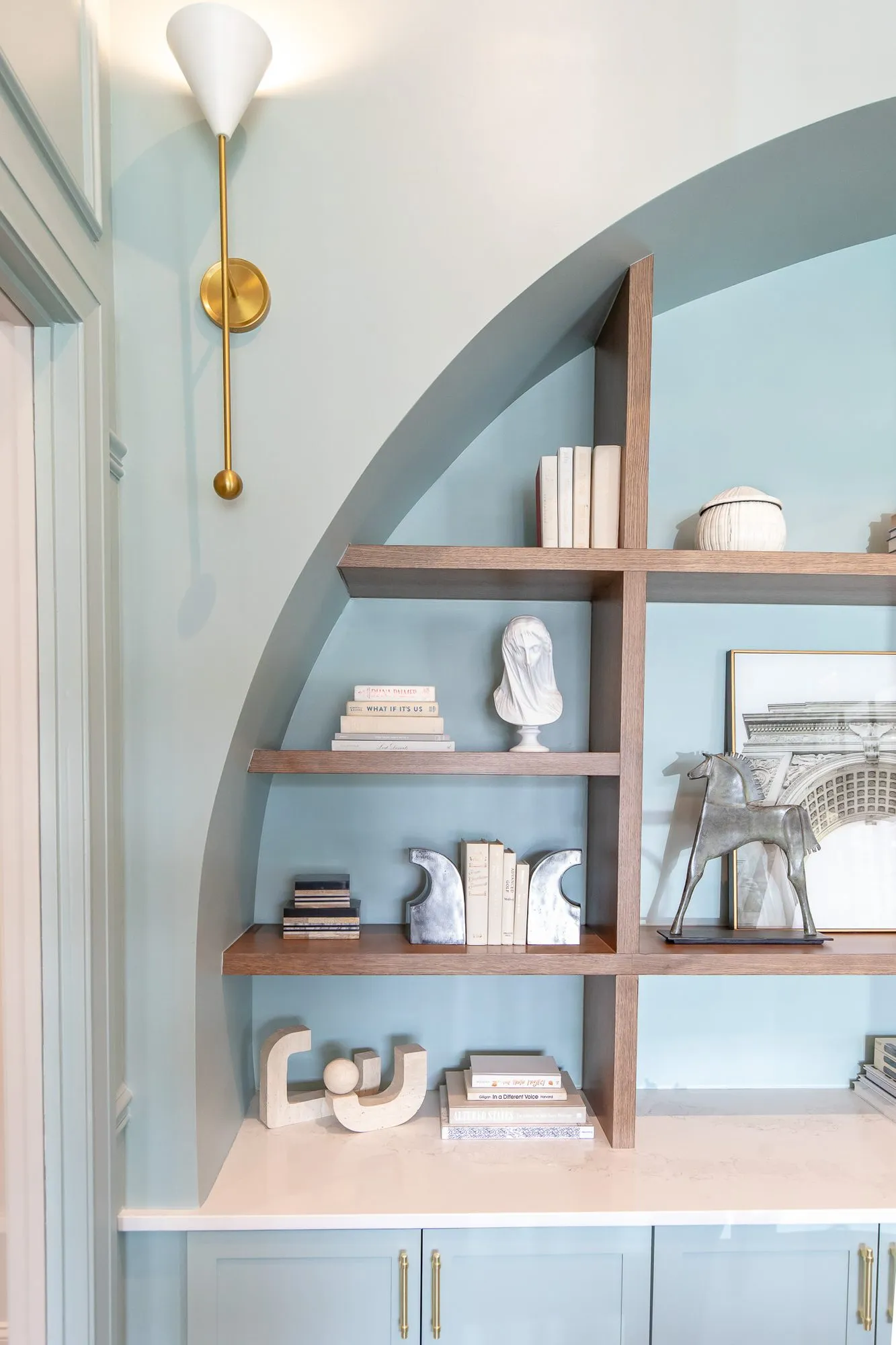 Multifamily amenity leasing office with an arched pale blue niche of walnut shelves, books, busts and sculptures