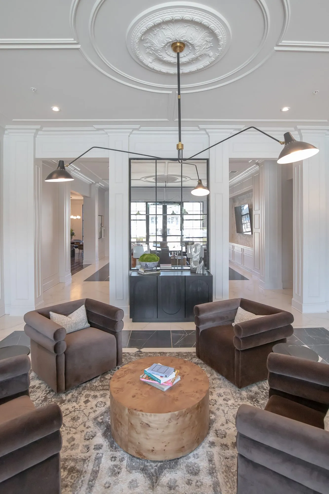 Multifamily amenity lobby lounge with brown velvet barrel chairs around a burl drum table under a black arm light