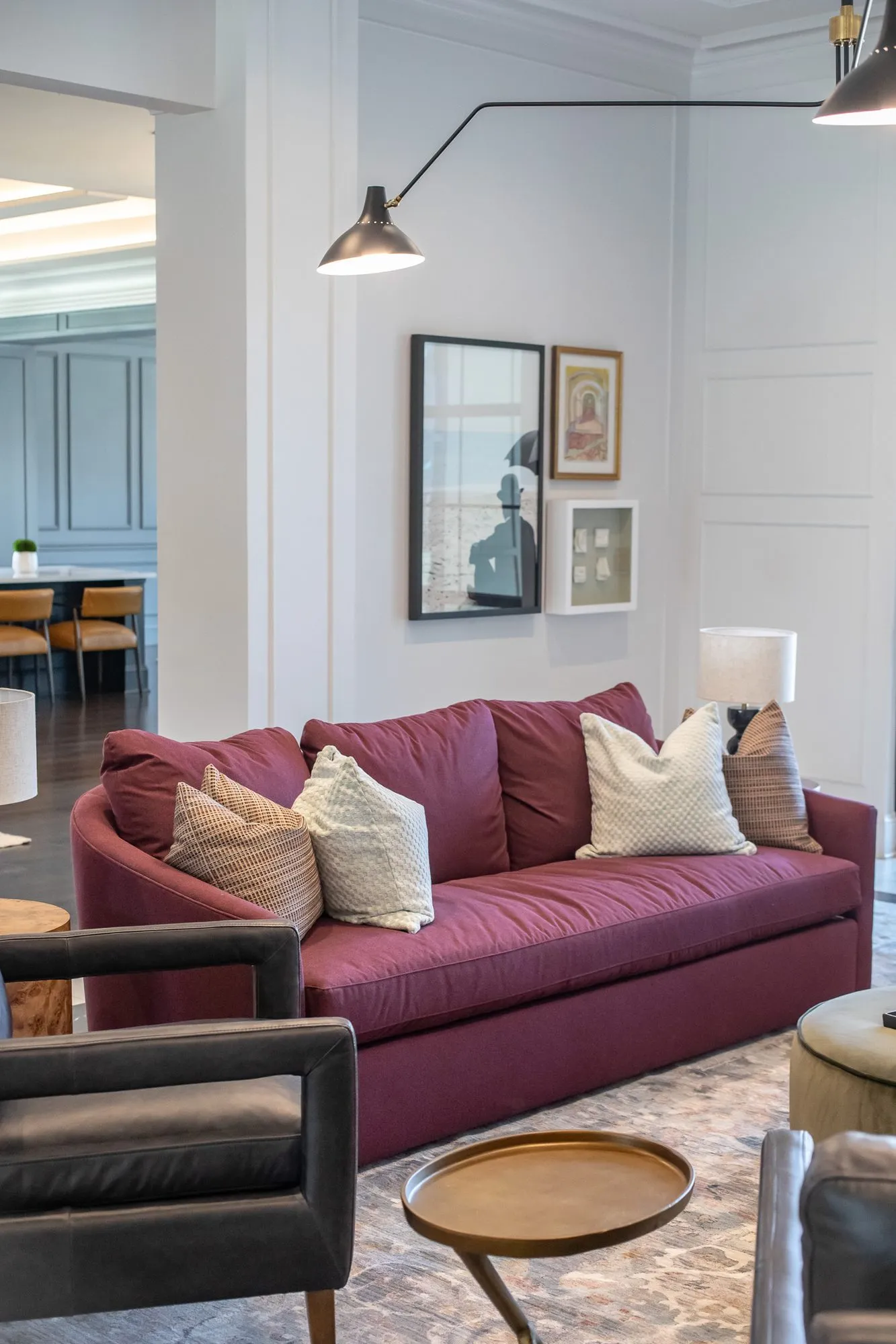 Multifamily amenity clubroom with a burgundy sofa, patterned pillows and a black leather armchair, framed prints on panelling