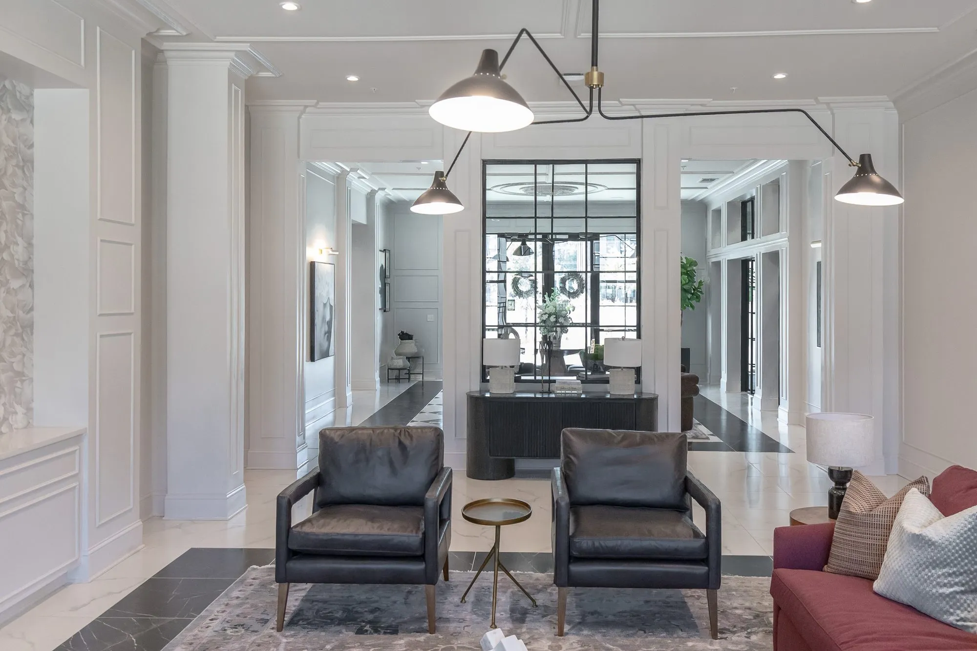 Multifamily amenity lounge with two black leather armchairs on a rug under a black arm light, a glazed doorway beyond