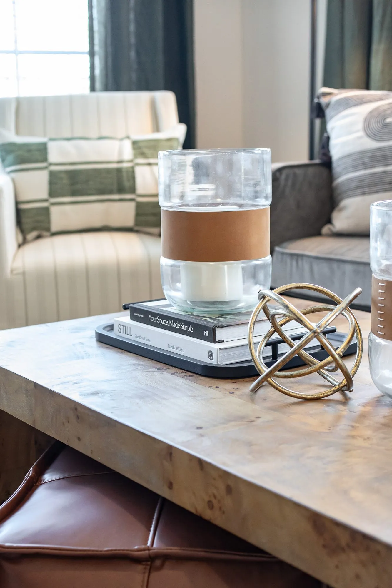 Multifamily amenity interior detail: burl wood coffee table with a glass candle holder, stacked books and a brass sphere