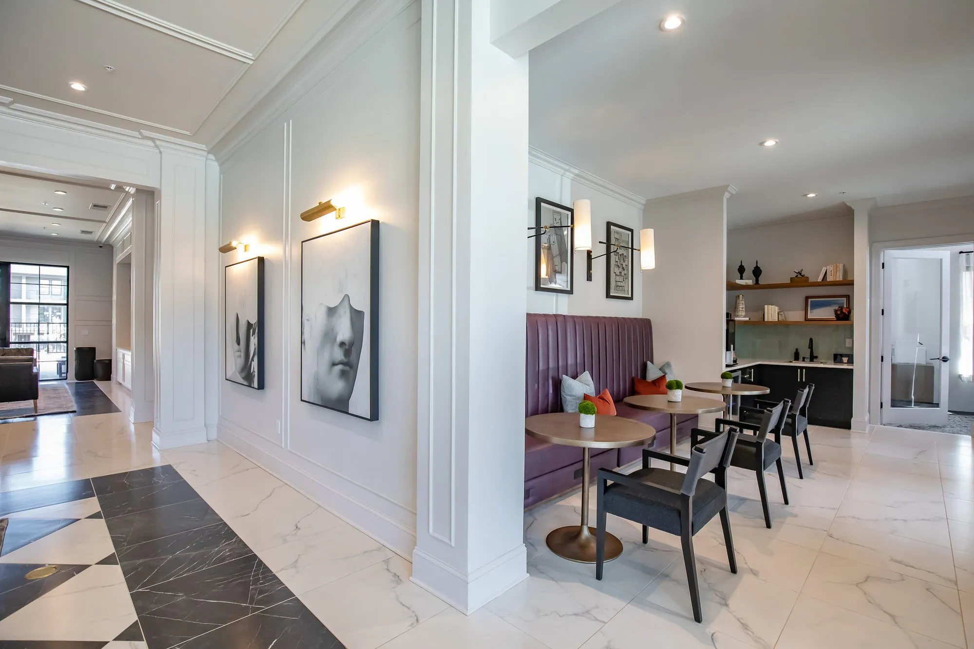 Multifamily amenity corridor opening to a plum banquette and cafe tables, framed face prints on white panelling