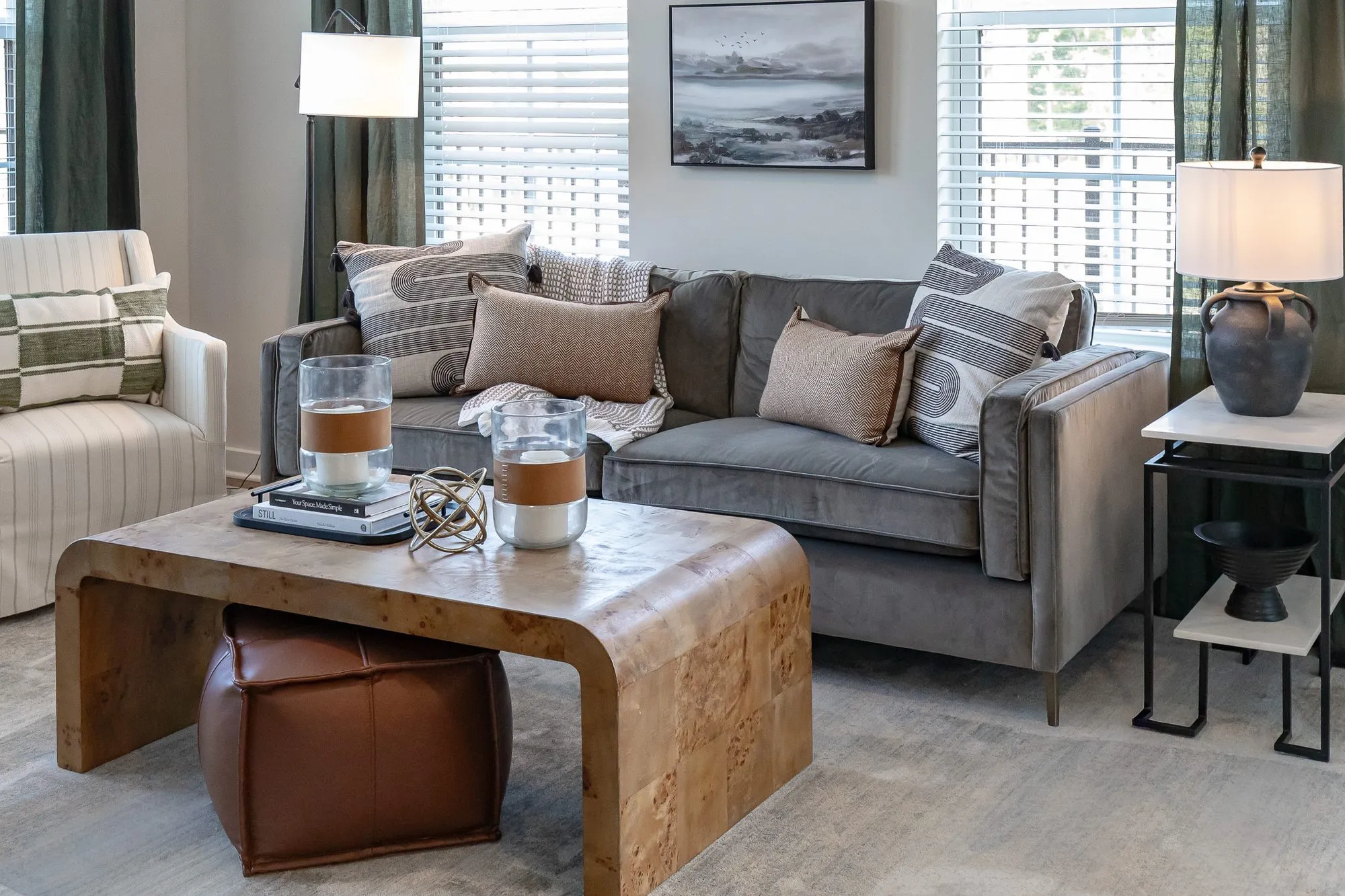 Multifamily apartment model living room with a grey velvet sofa, a burl waterfall coffee table and a striped armchair