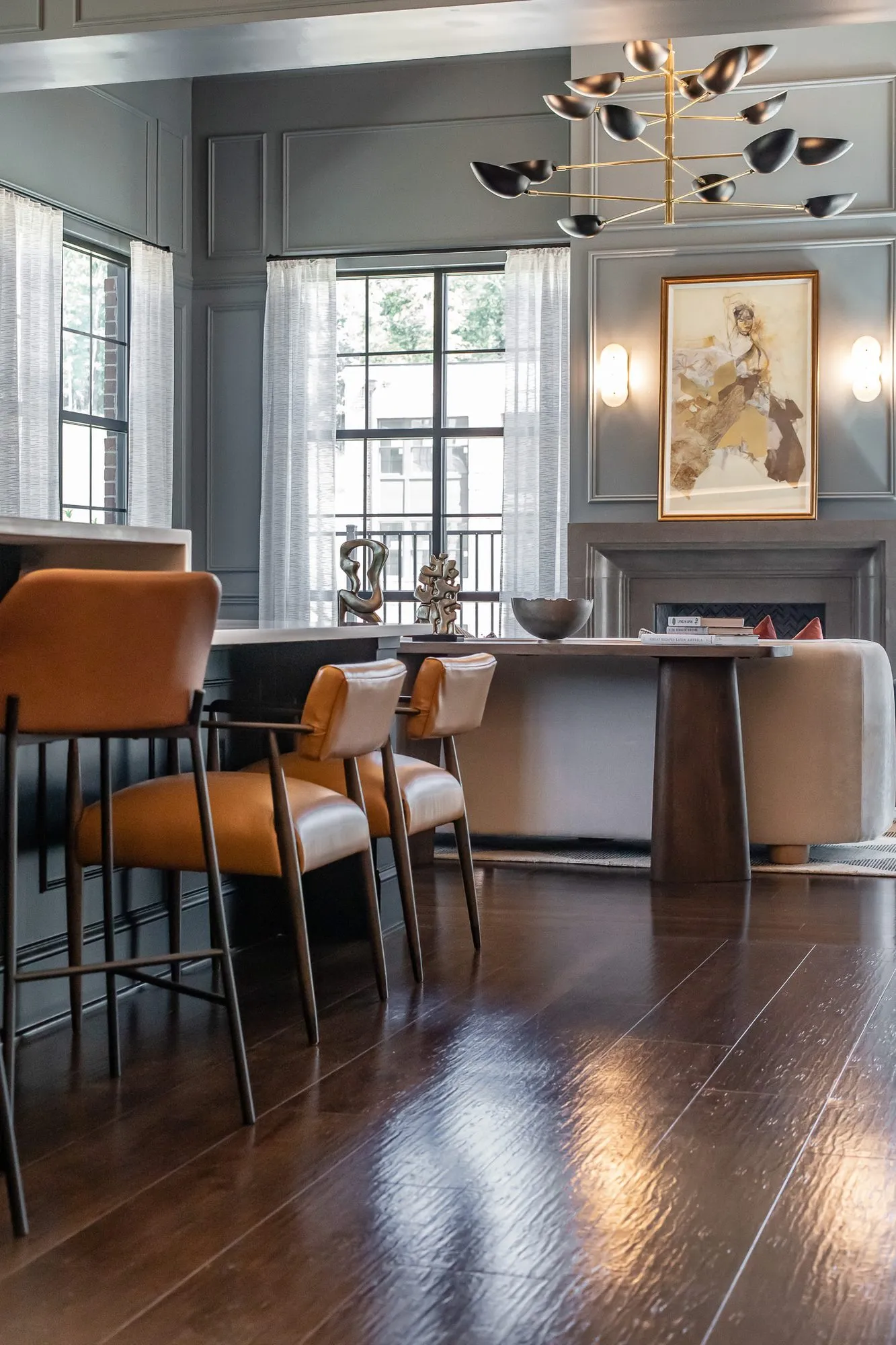 Multifamily amenity clubroom bar with cognac leather stools at a counter, a brass bird chandelier and fireplace beyond