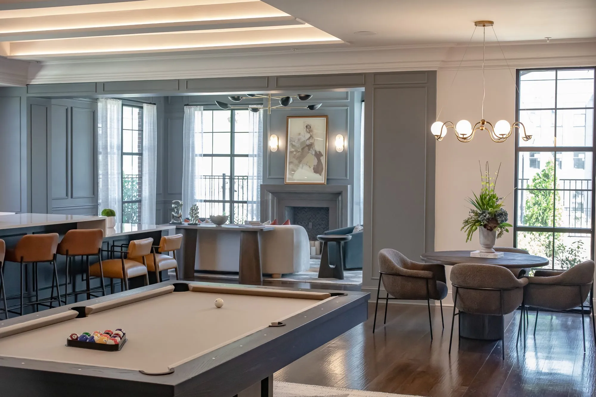 Multifamily amenity clubroom with a billiards table before cognac bar stools and grey dining chairs, a chandelier beyond
