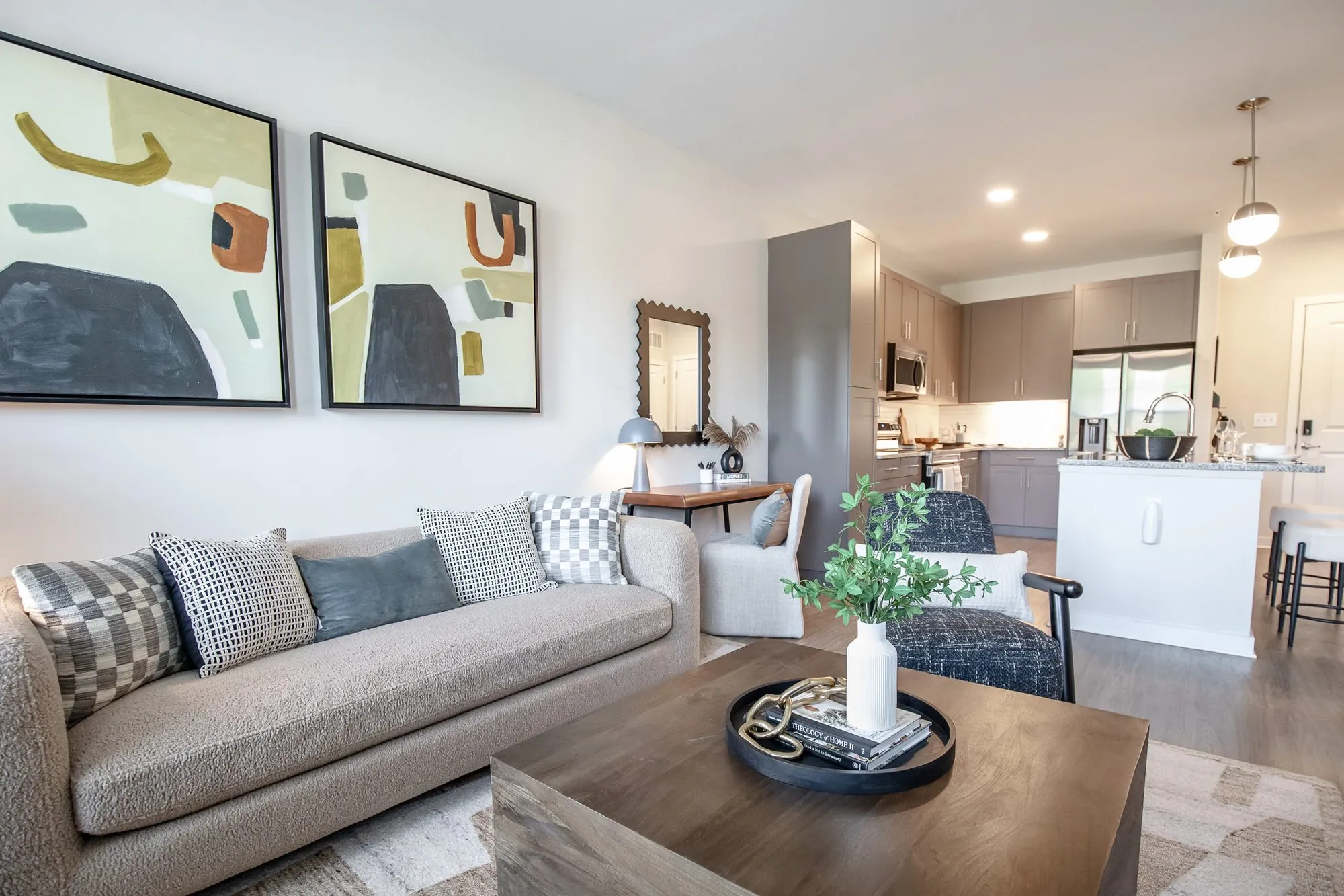 Multifamily apartment model, open plan with a taupe sofa below two abstract prints and the kitchen beyond
