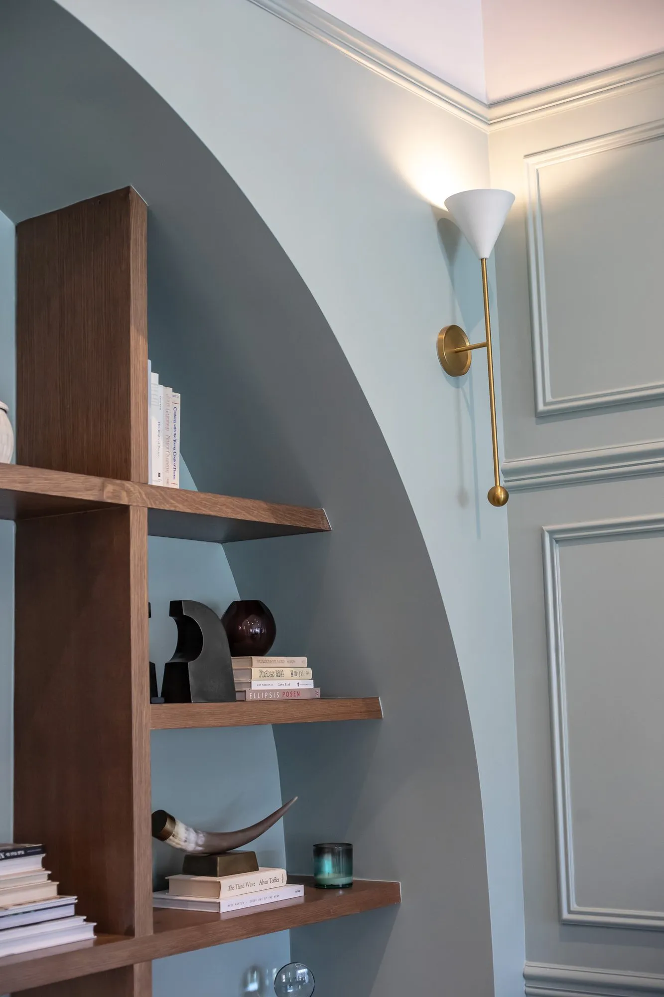 Multifamily amenity leasing office with an arched pale blue niche of walnut shelves beside a brass torch sconce
