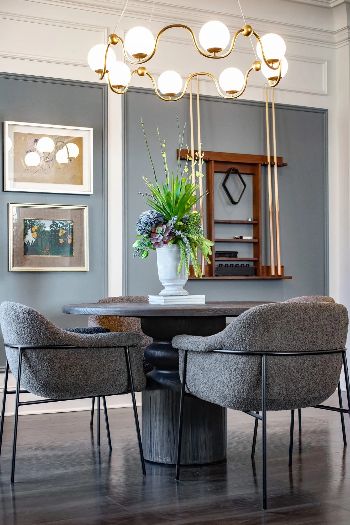 Multifamily amenity clubroom with grey boucle chairs at a round table under a brass globe chandelier, an orchid on top