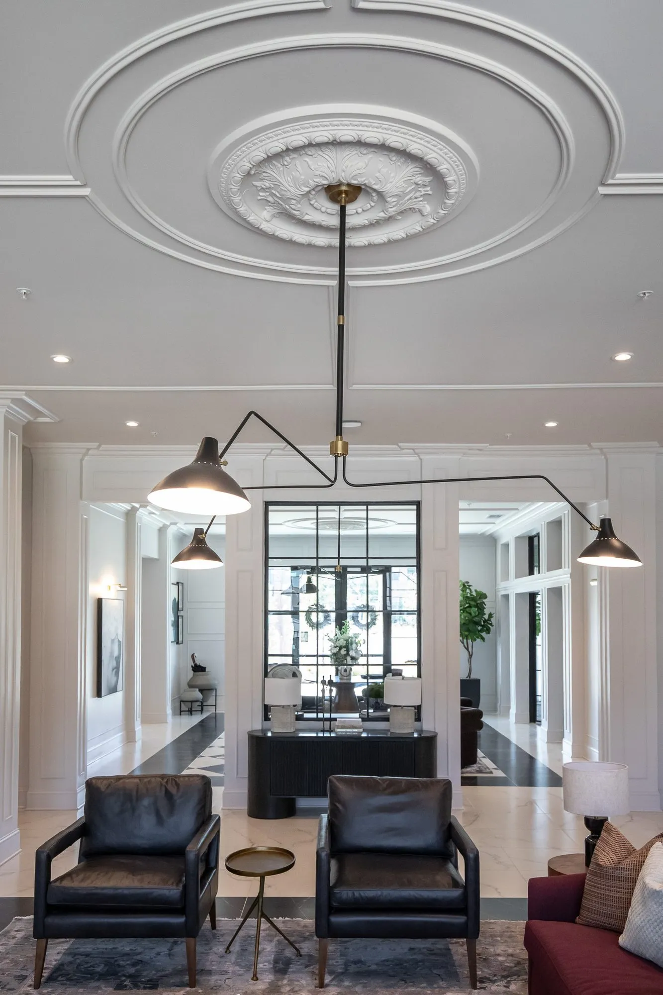 Multifamily amenity lounge with two black leather armchairs under a black arm light and ceiling medallion, a glazed entry