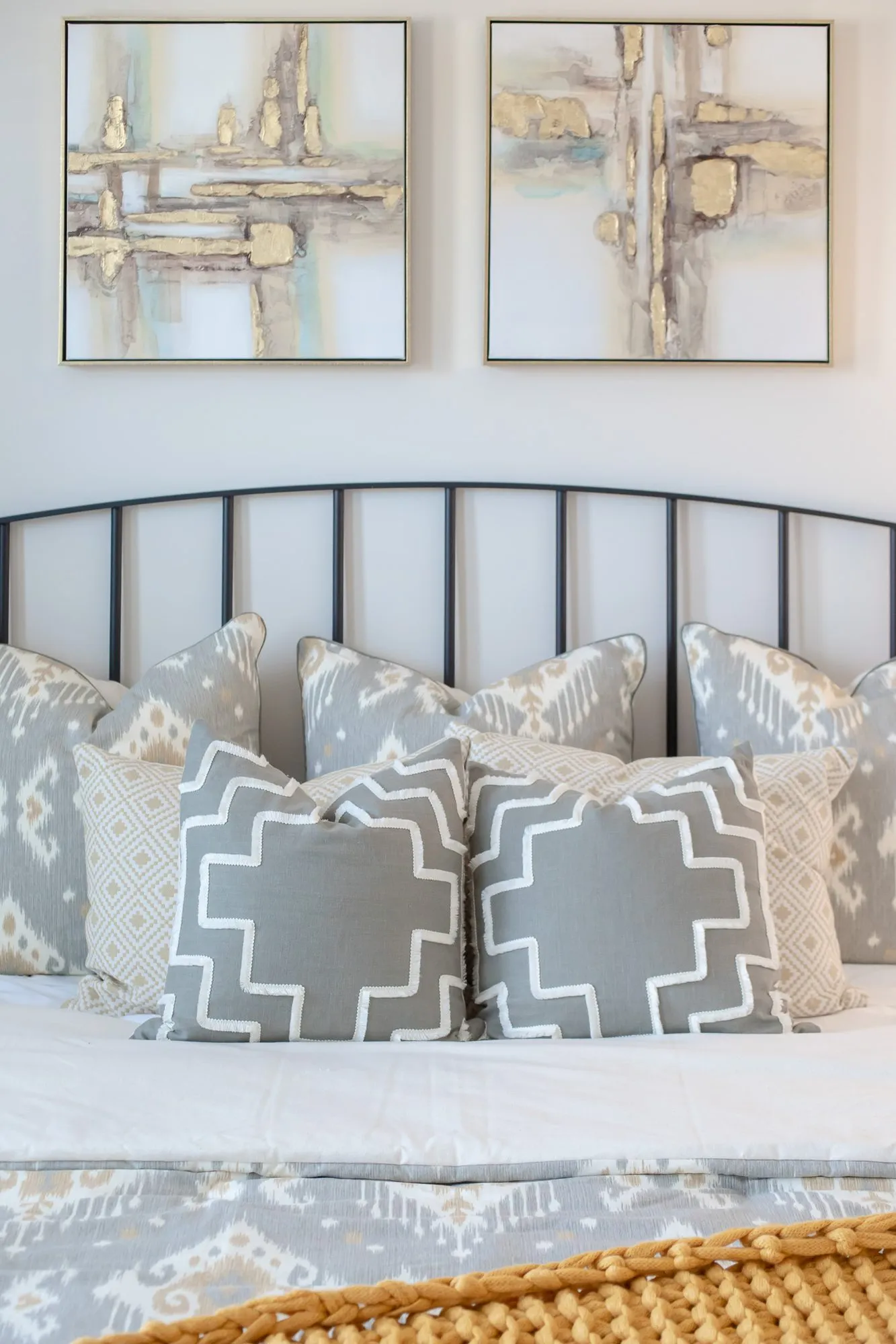 Multifamily apartment bedroom with a black spindle headboard and patterned pillows below two abstract prints in gold and grey