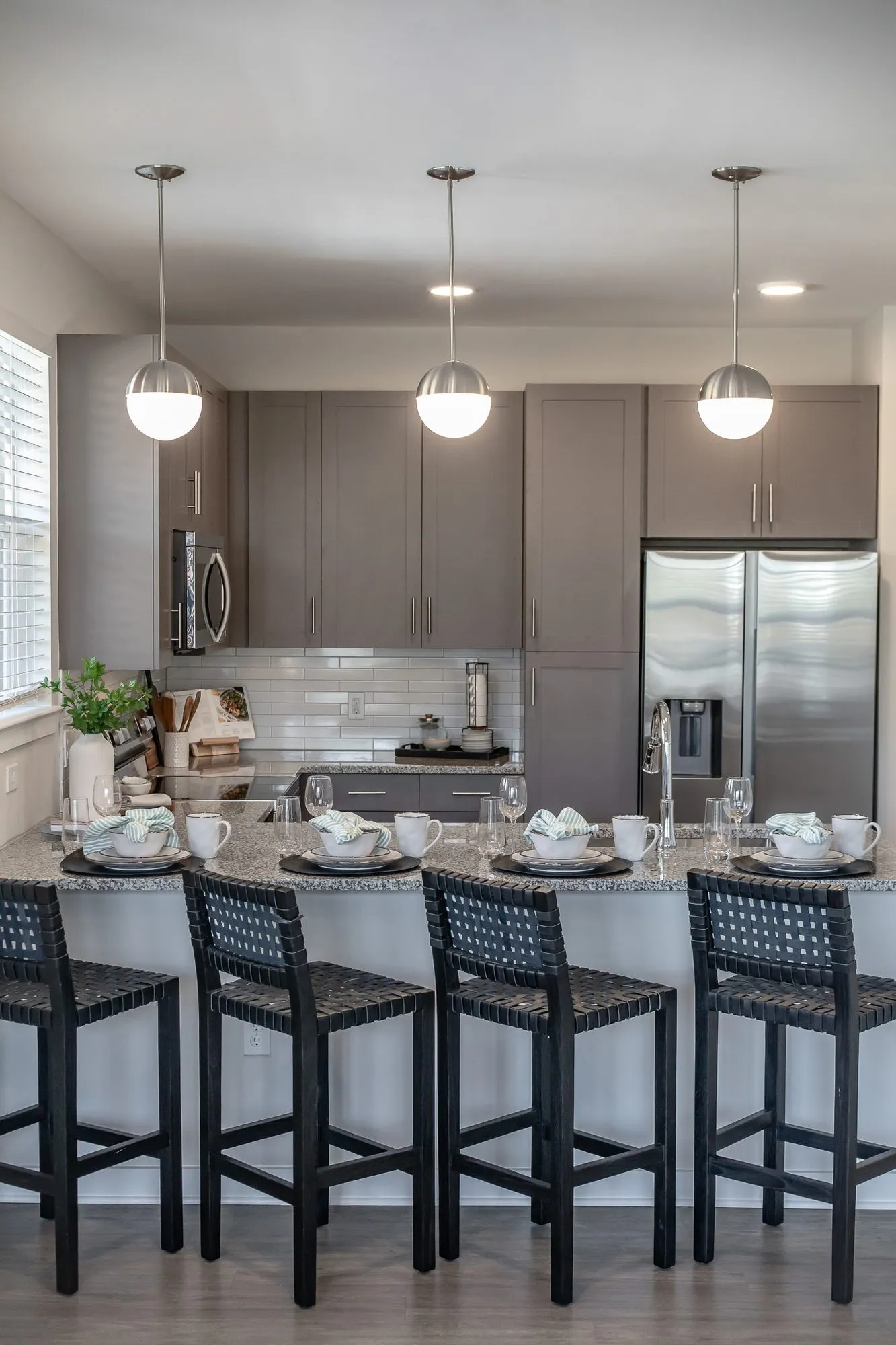 Multifamily apartment model kitchen with grey cabinets, globe pendants and black woven leather stools at a set island
