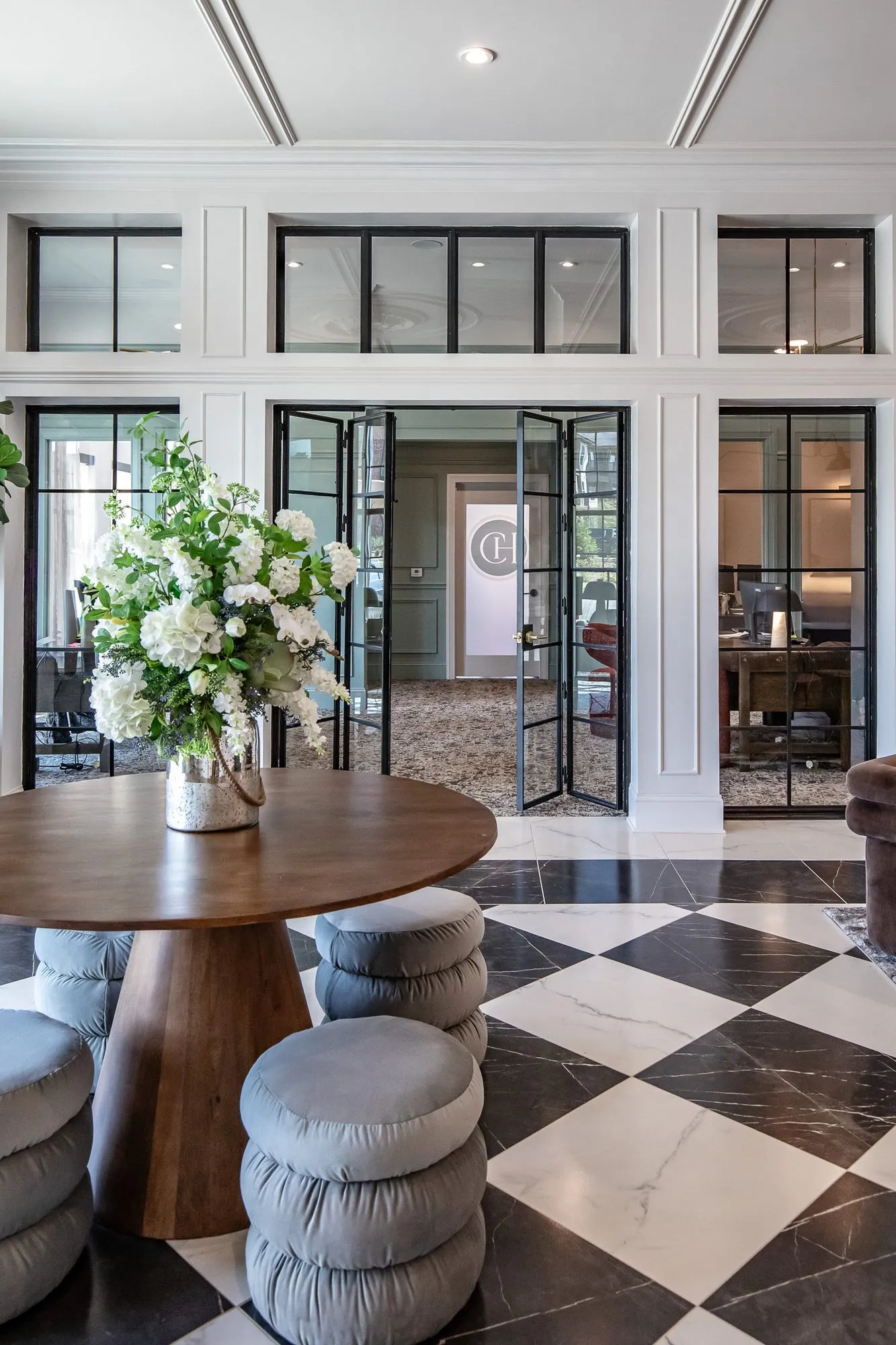 Multifamily amenity lobby with a round wood table of white flowers and grey puff stools on checkerboard marble