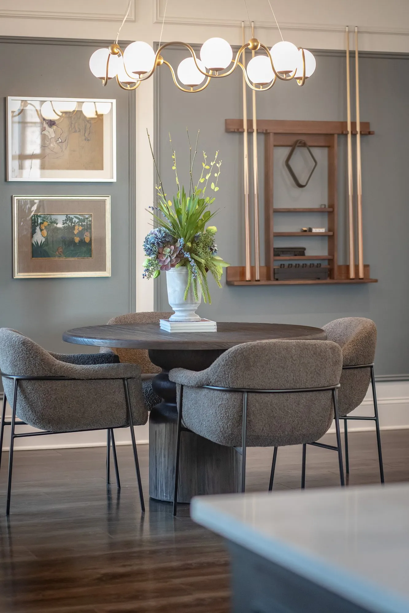 Multifamily amenity clubroom with a cue rack on grey panelling behind a round table and boucle chairs under a chandelier