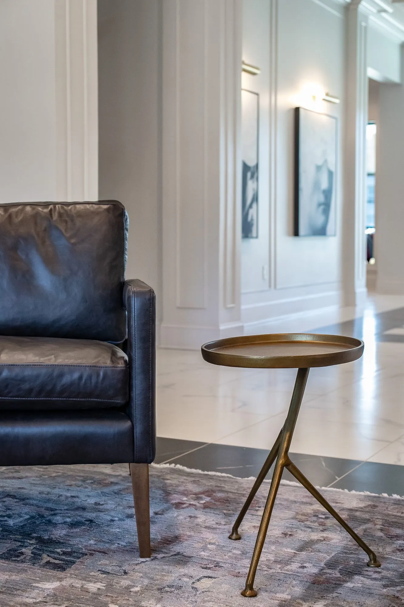 Multifamily amenity interior detail: black leather armchair and brass tripod side table on a patterned rug, white panelling