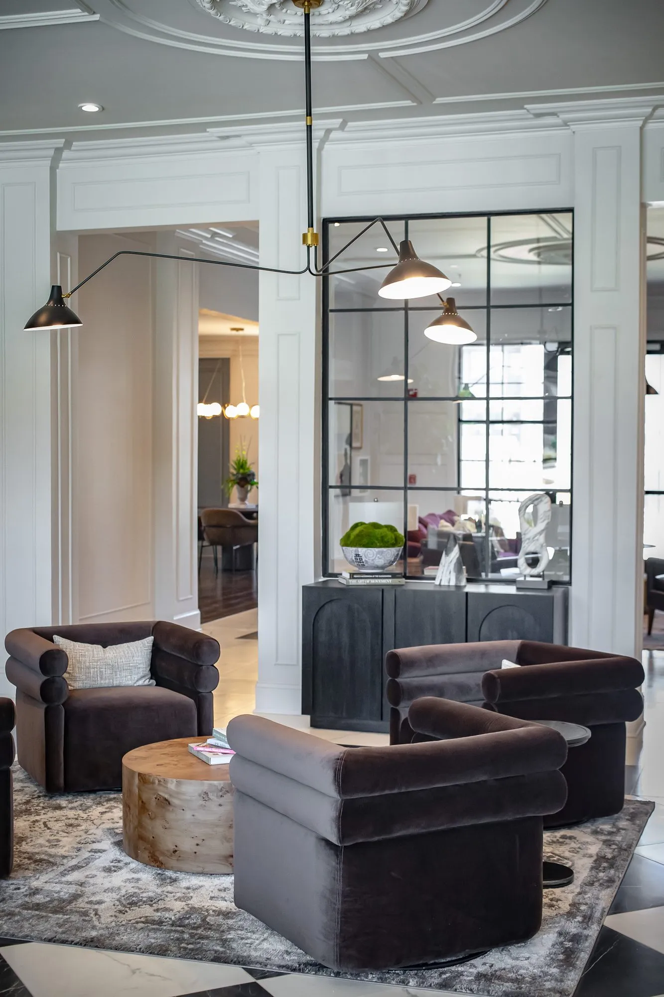 Multifamily amenity lobby lounge with brown velvet swivel chairs around a burl table, a black grid mirror and console beyond