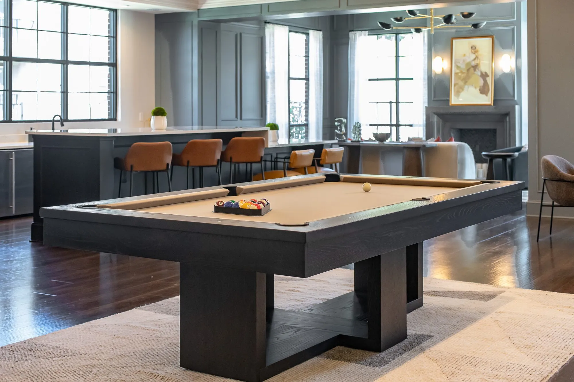 Multifamily amenity clubroom with a billiards table before the long bar with cognac stools and a fireplace beyond