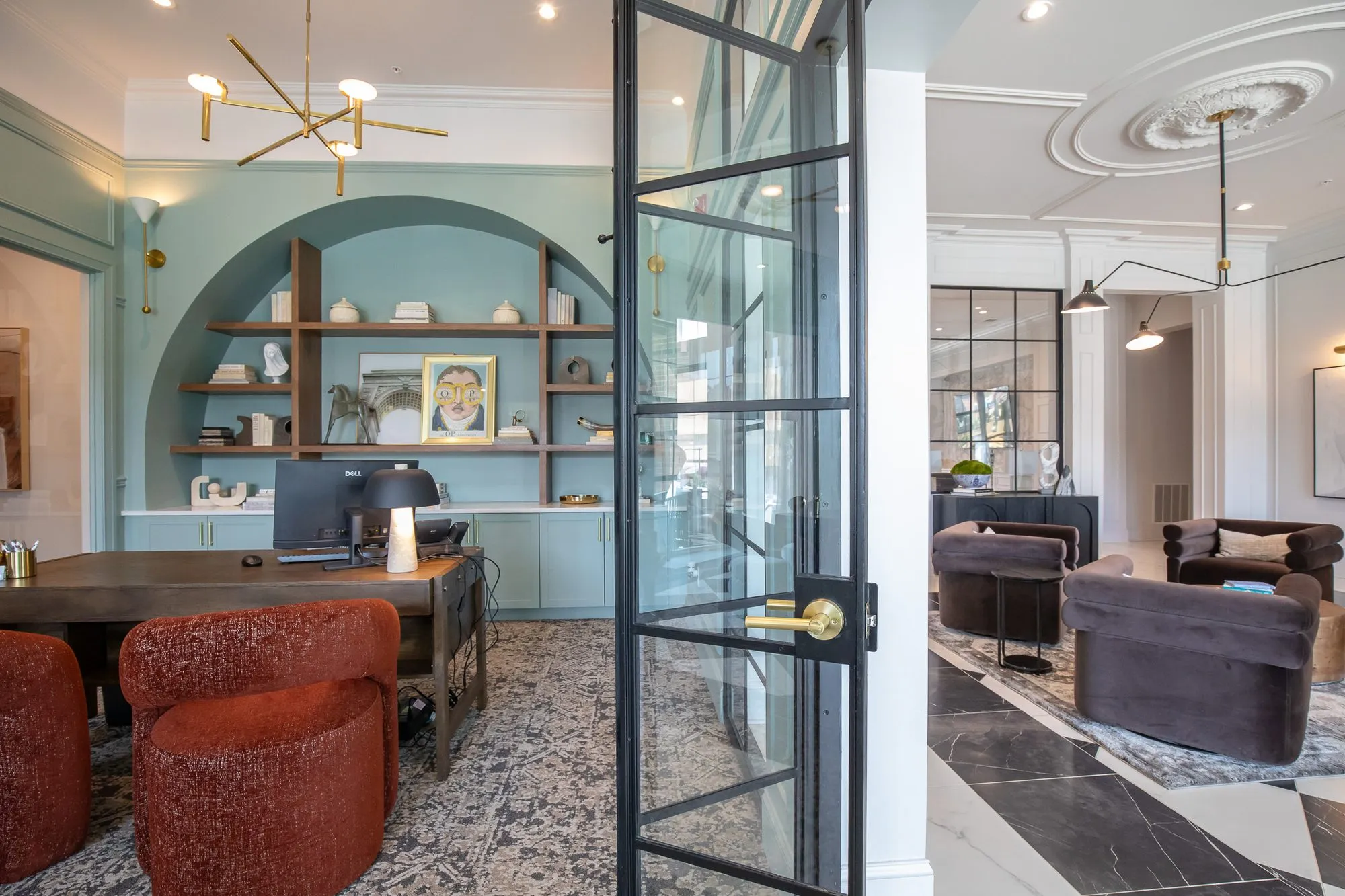 Multifamily amenity leasing office with rust boucle chairs at a desk before an arched blue niche, a steel door to the lobby