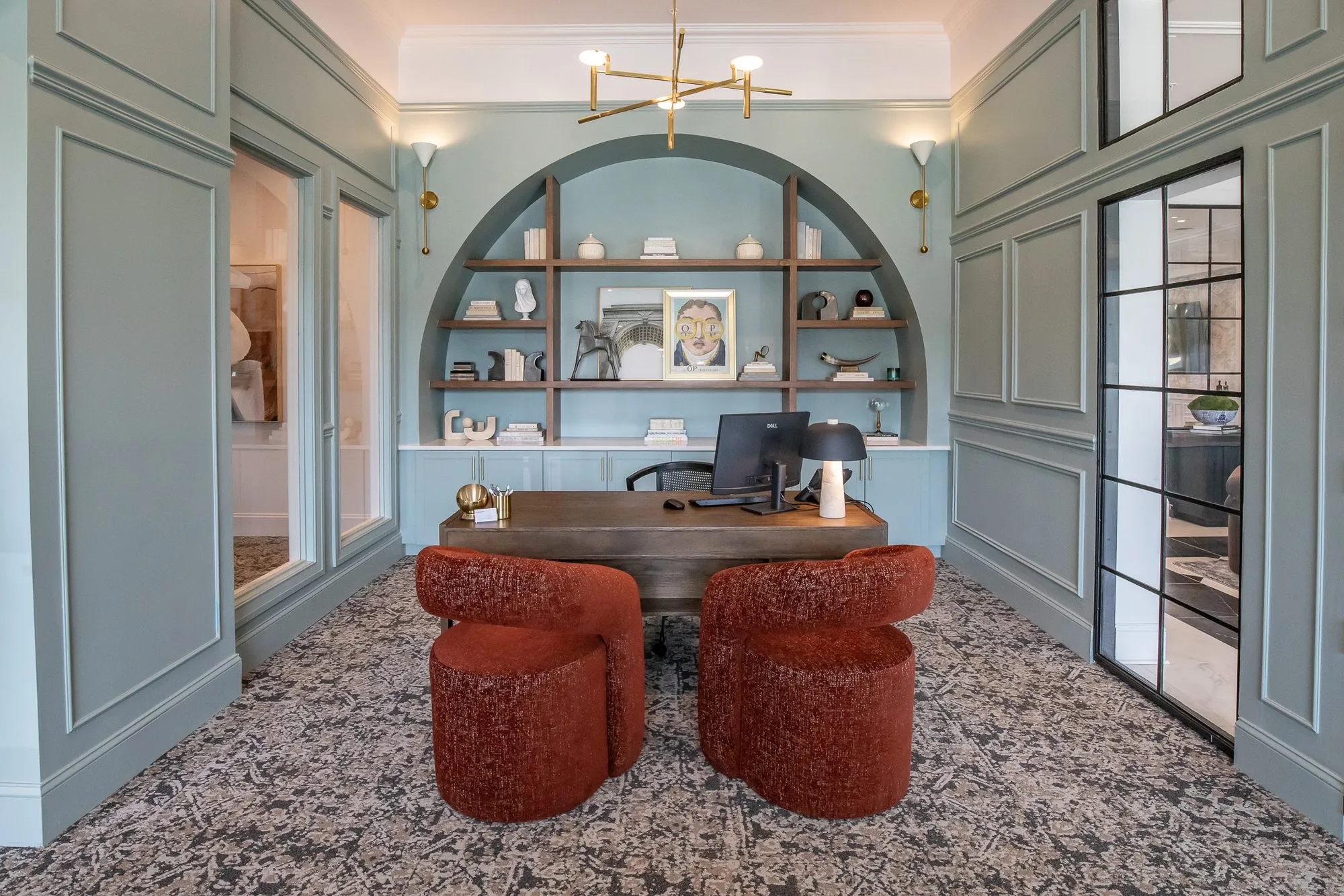 Multifamily amenity leasing office with rust boucle chairs at a wood desk before an arched niche in pale blue panelling