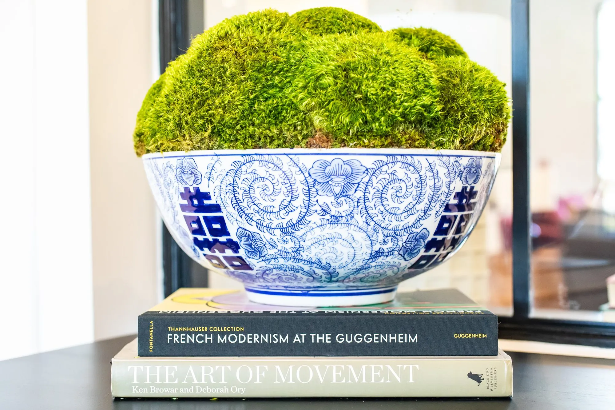 Multifamily interior detail: blue and white porcelain bowl of moss on a stack of art books