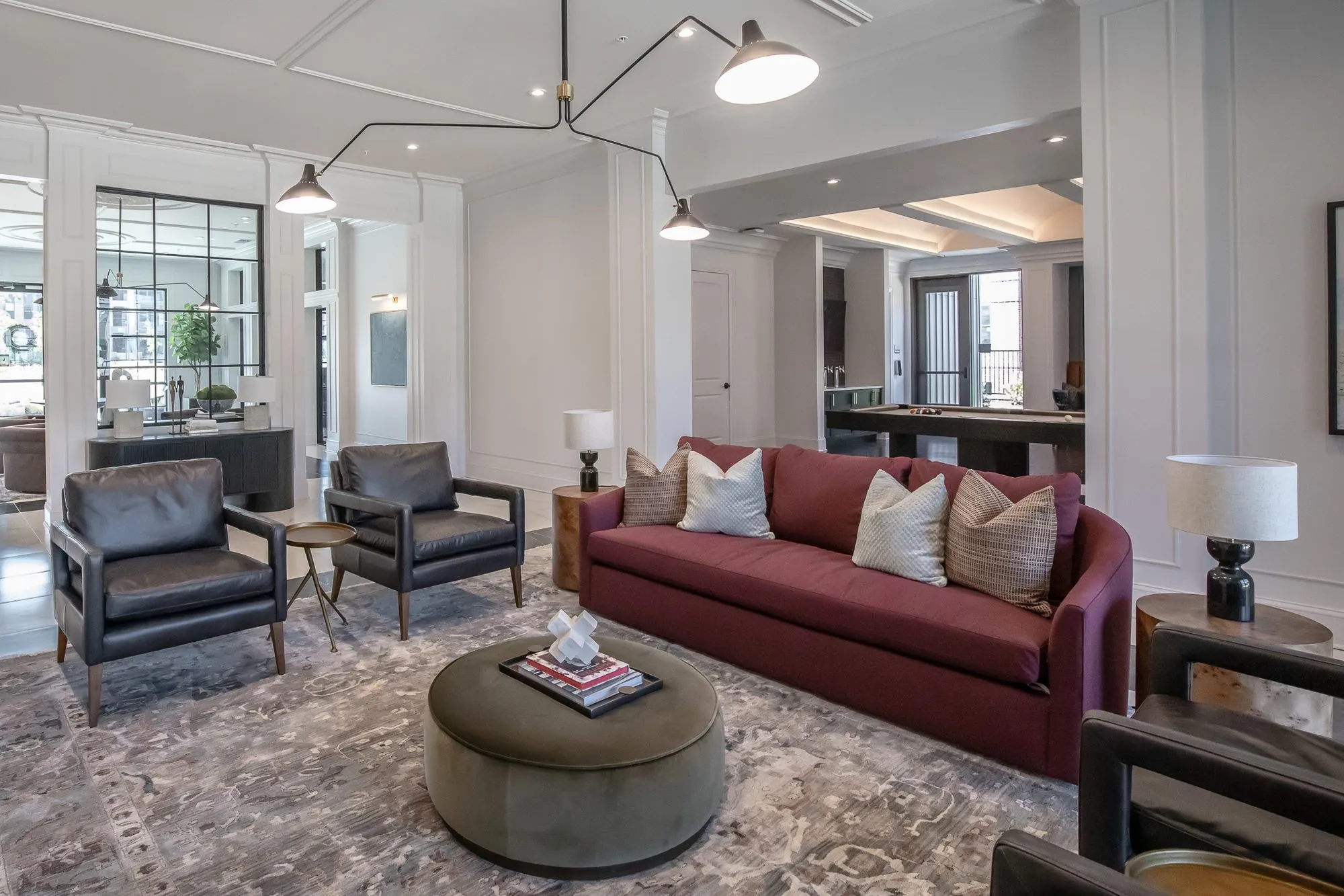 Multifamily amenity clubroom with a burgundy sofa, black leather armchairs and an olive ottoman under a black arm light