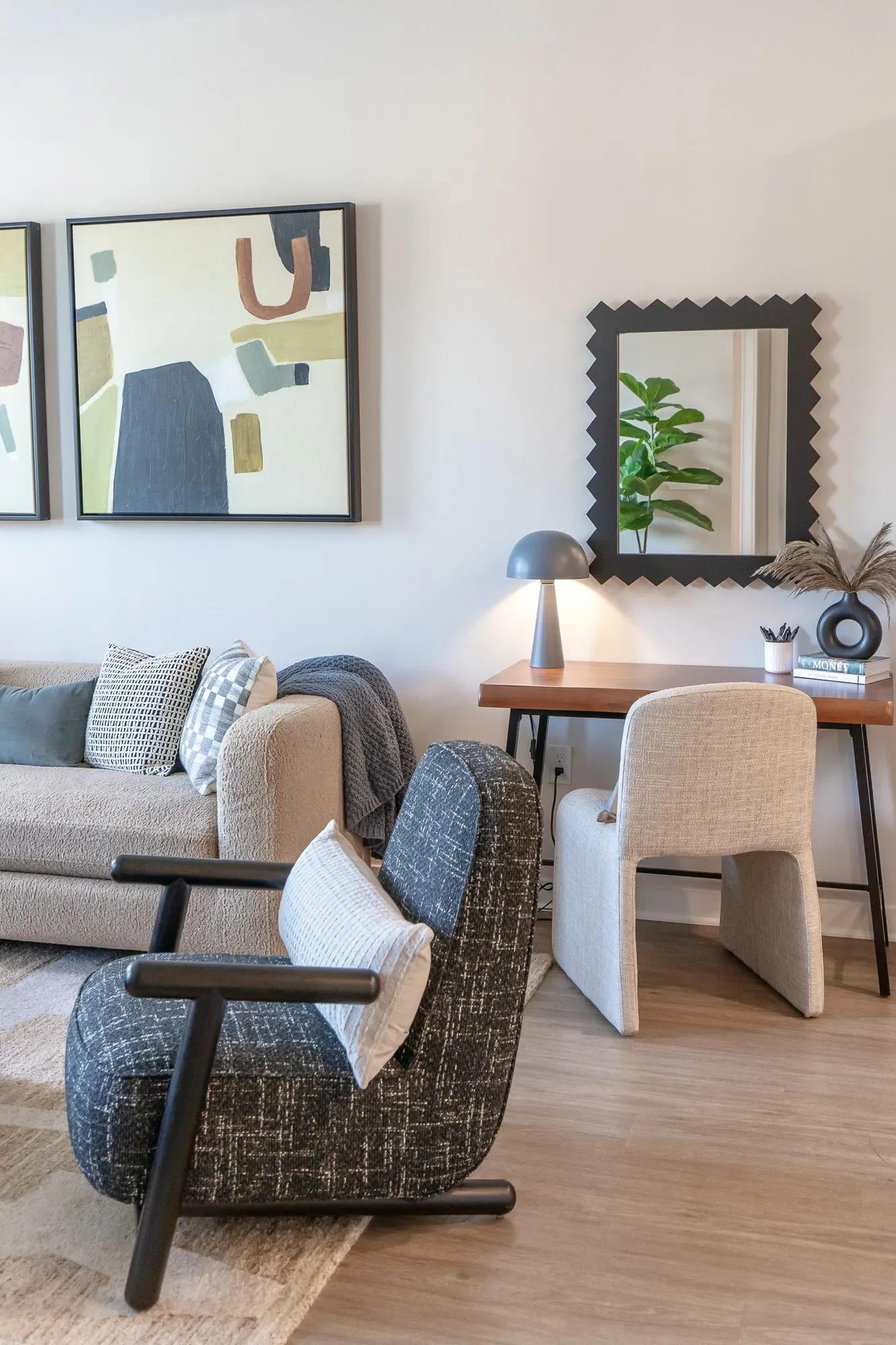 Multifamily apartment model living room with a taupe sofa and black patterned armchair, a desk with a mushroom lamp