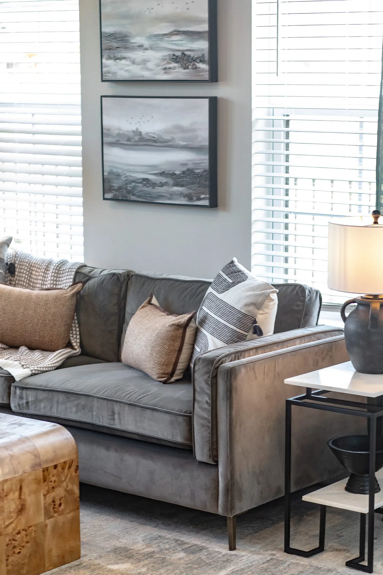 Multifamily apartment model living room with a grey velvet sofa and patterned pillows below two framed seascape prints