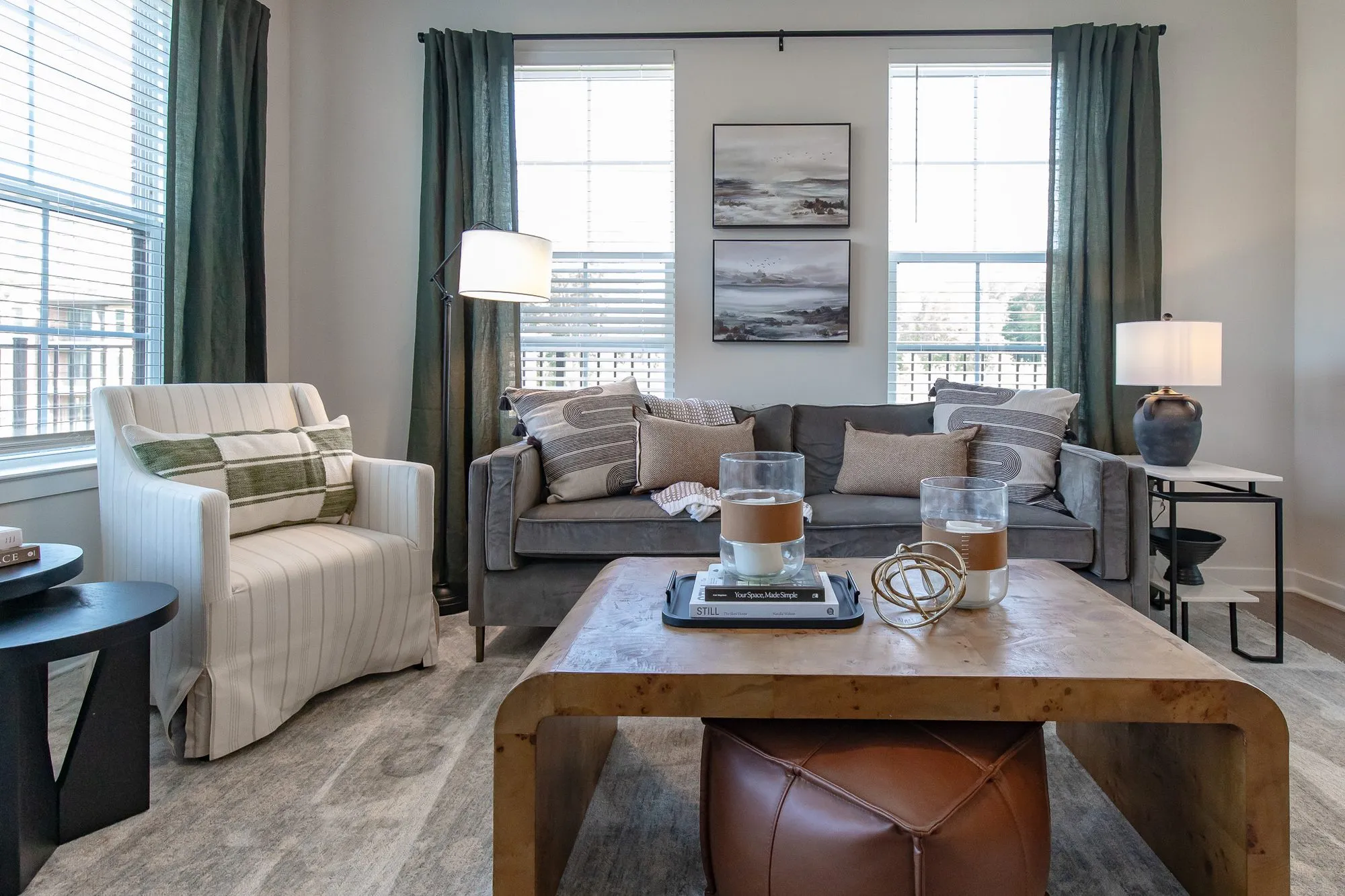 Multifamily apartment model living room with a grey velvet sofa, a burl waterfall coffee table and a striped armchair