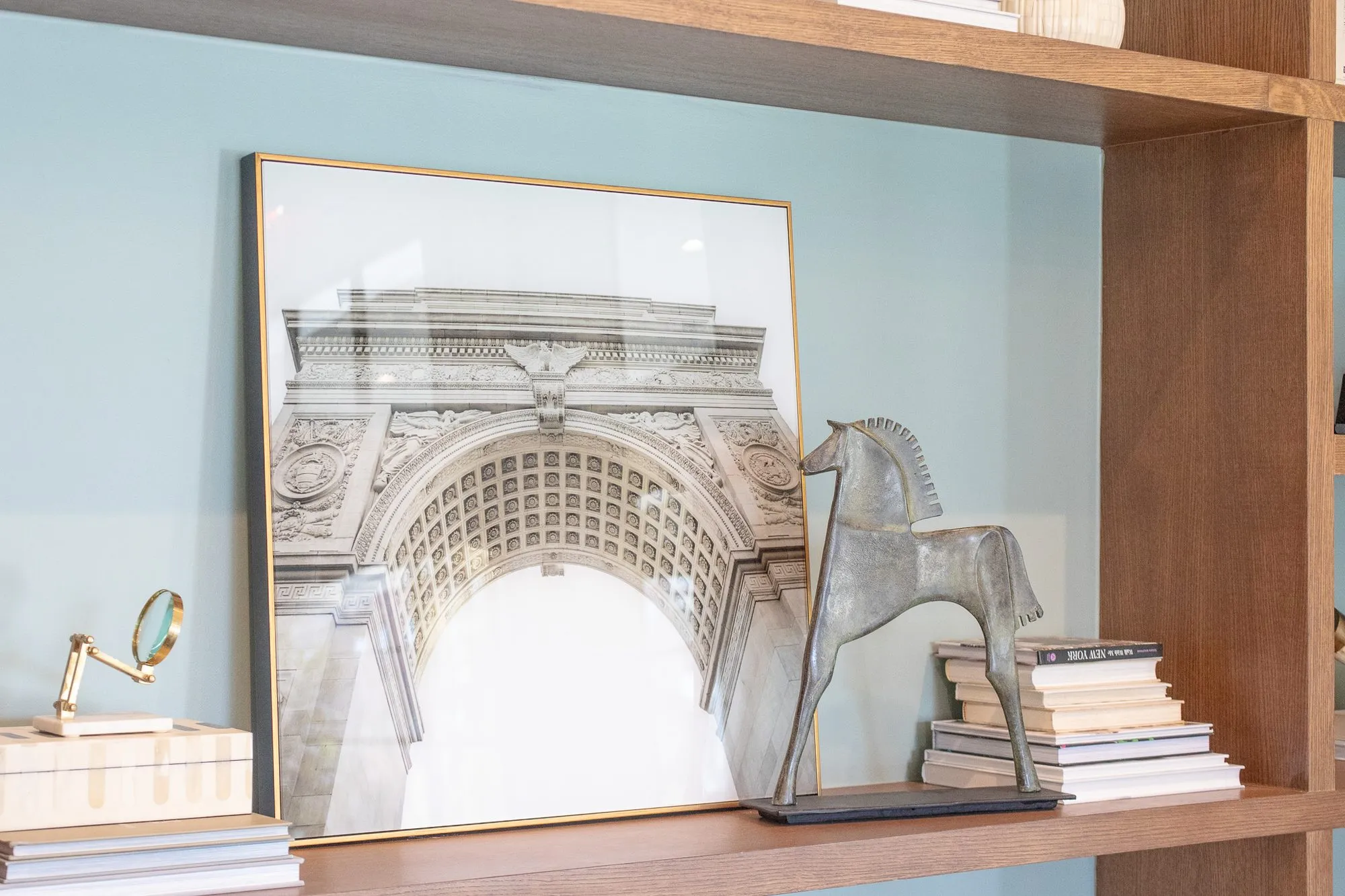 Multifamily interior detail: shelf with a classical arch print, a bronze horse figure, stacked books and a brass magnifier