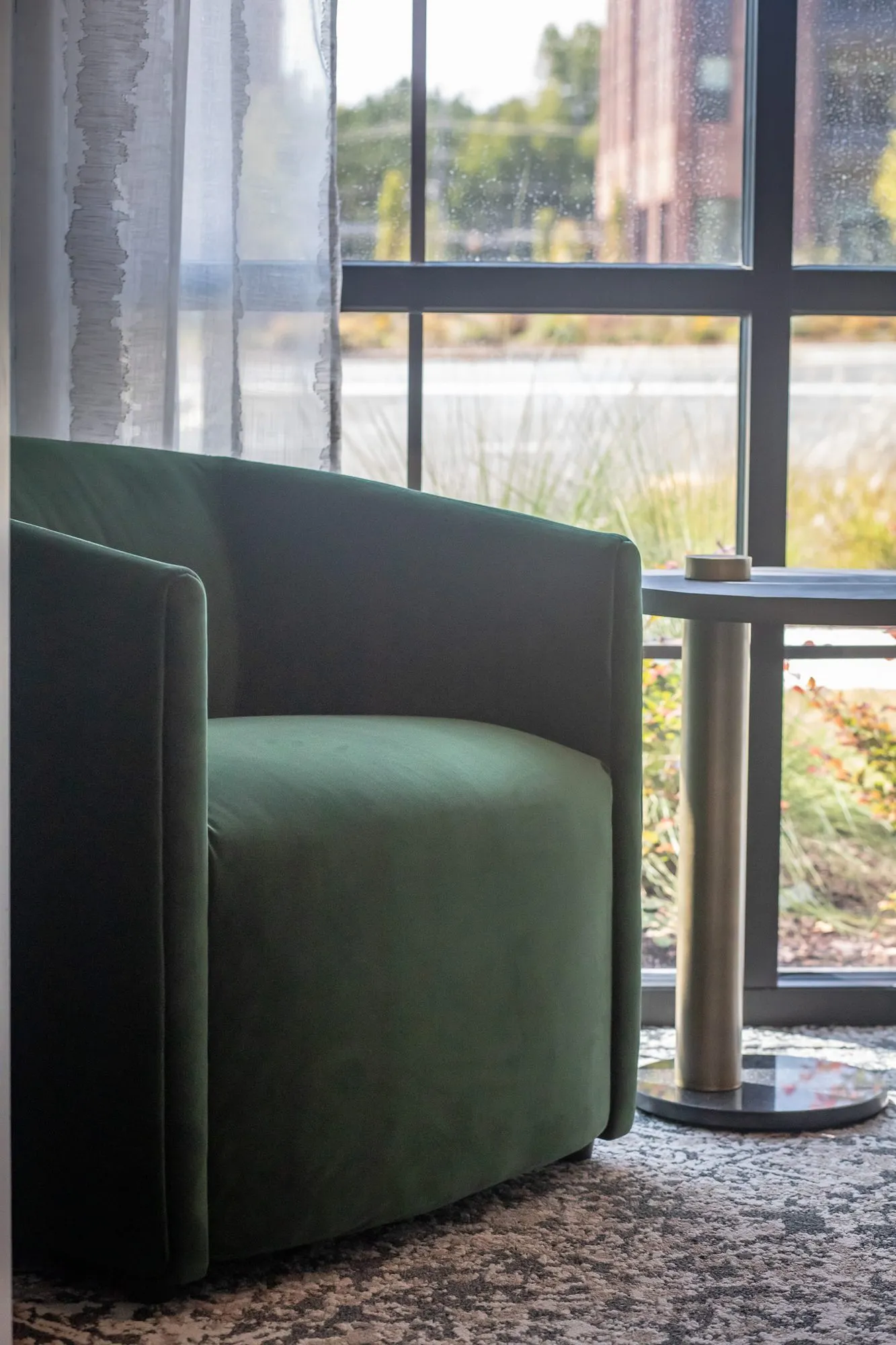 Multifamily amenity interior detail: dark green velvet swivel chair and a side table by a tall black framed window