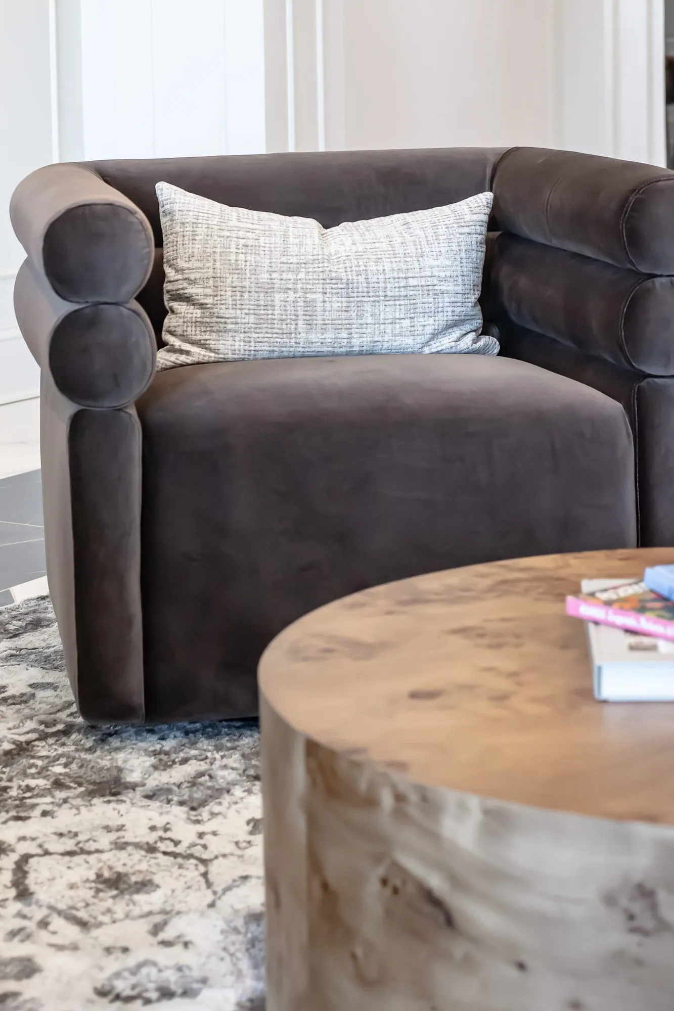 Multifamily amenity interior detail: brown channel-back velvet chair with a woven pillow beside a burl drum table