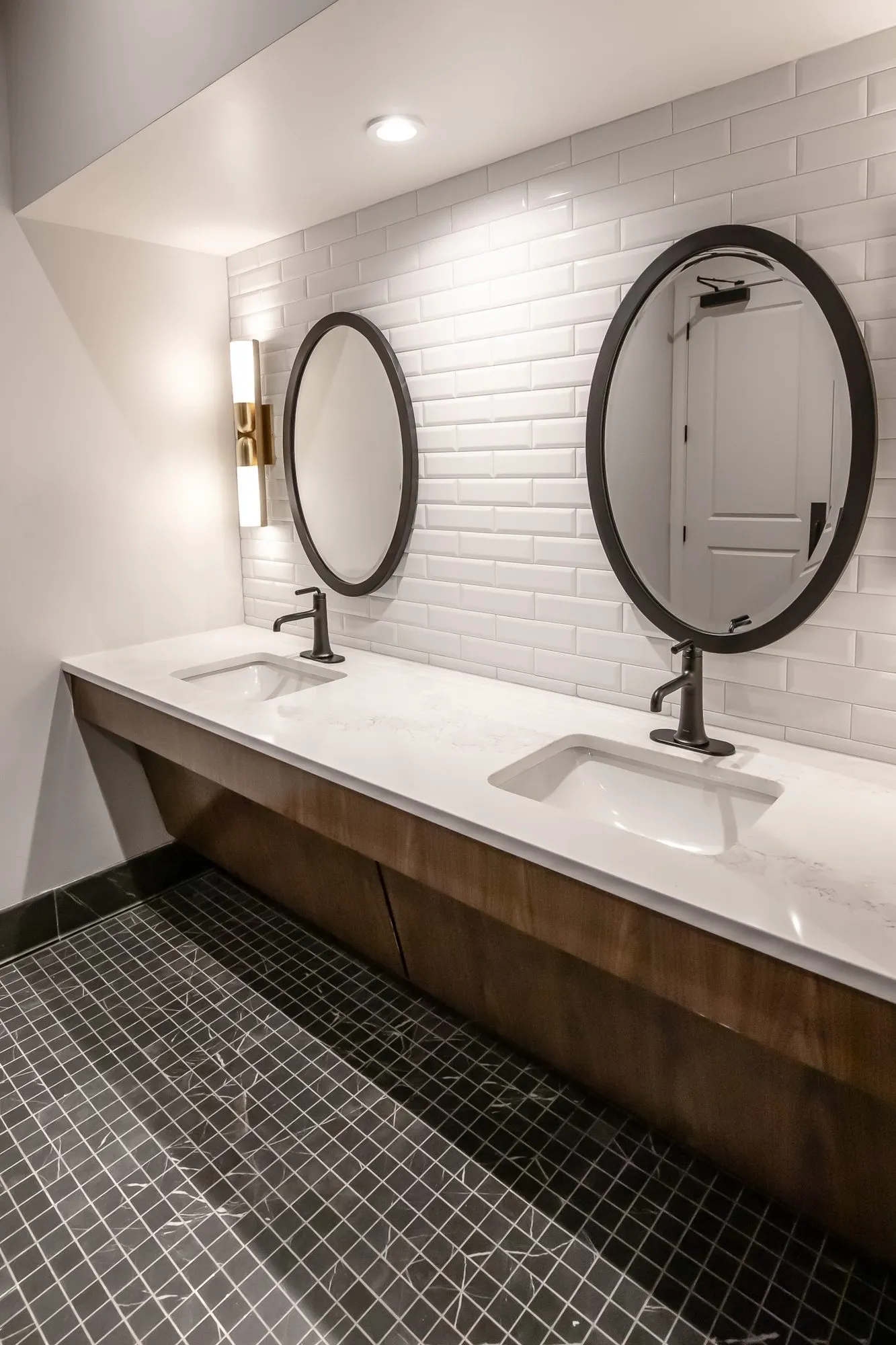 Multifamily amenity restroom with two oval black-framed mirrors on white subway tile above a floating vanity, mosaic floor