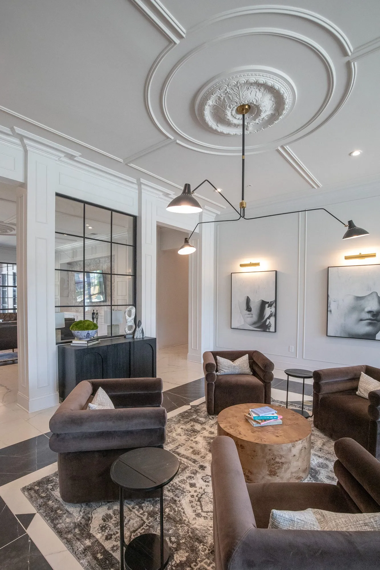 Multifamily amenity lobby lounge with brown velvet chairs around a burl table under a black arm light and plaster medallion