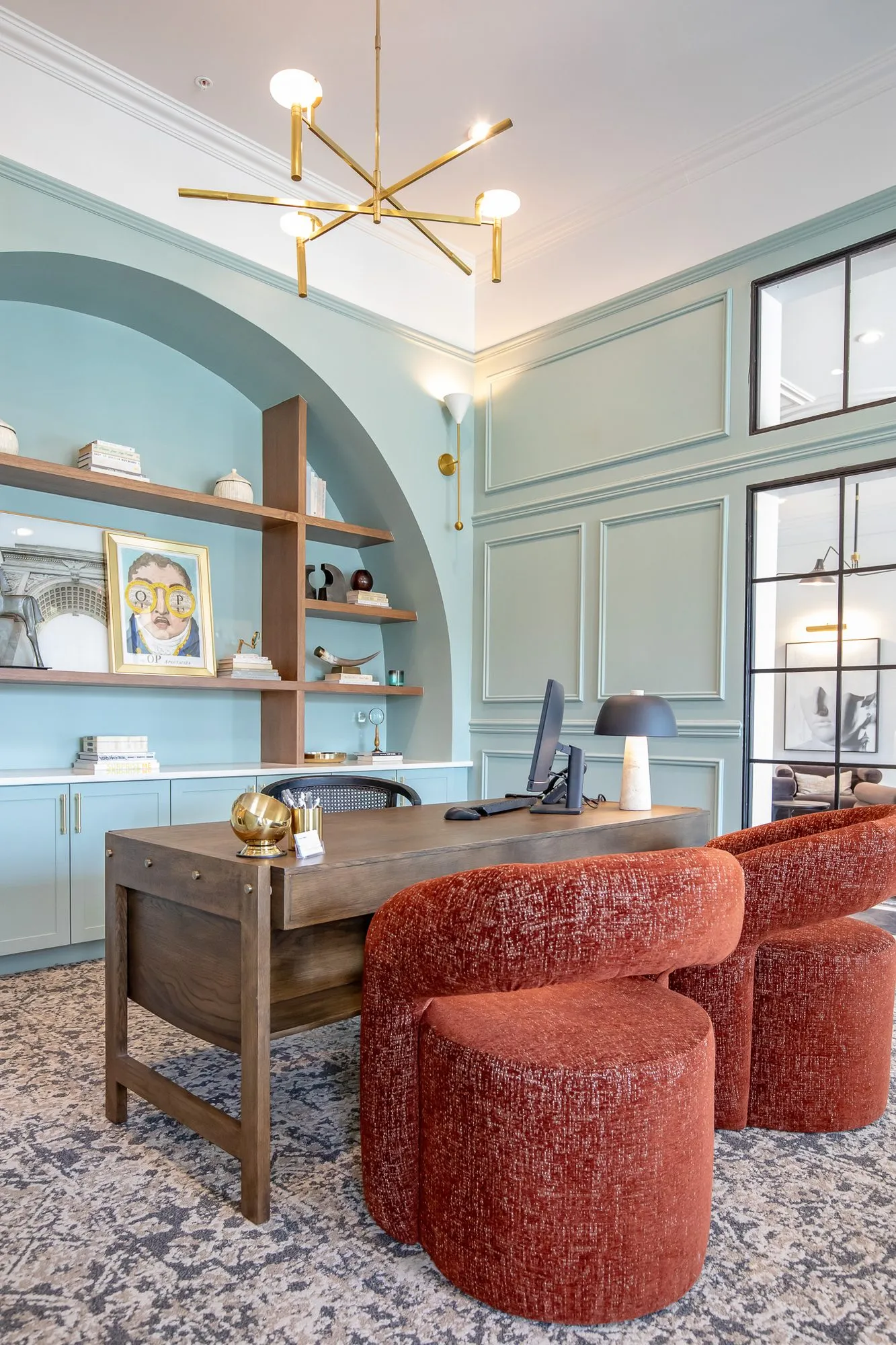 Multifamily amenity leasing office with rust boucle chairs at a wood desk before a pale blue arched shelf niche