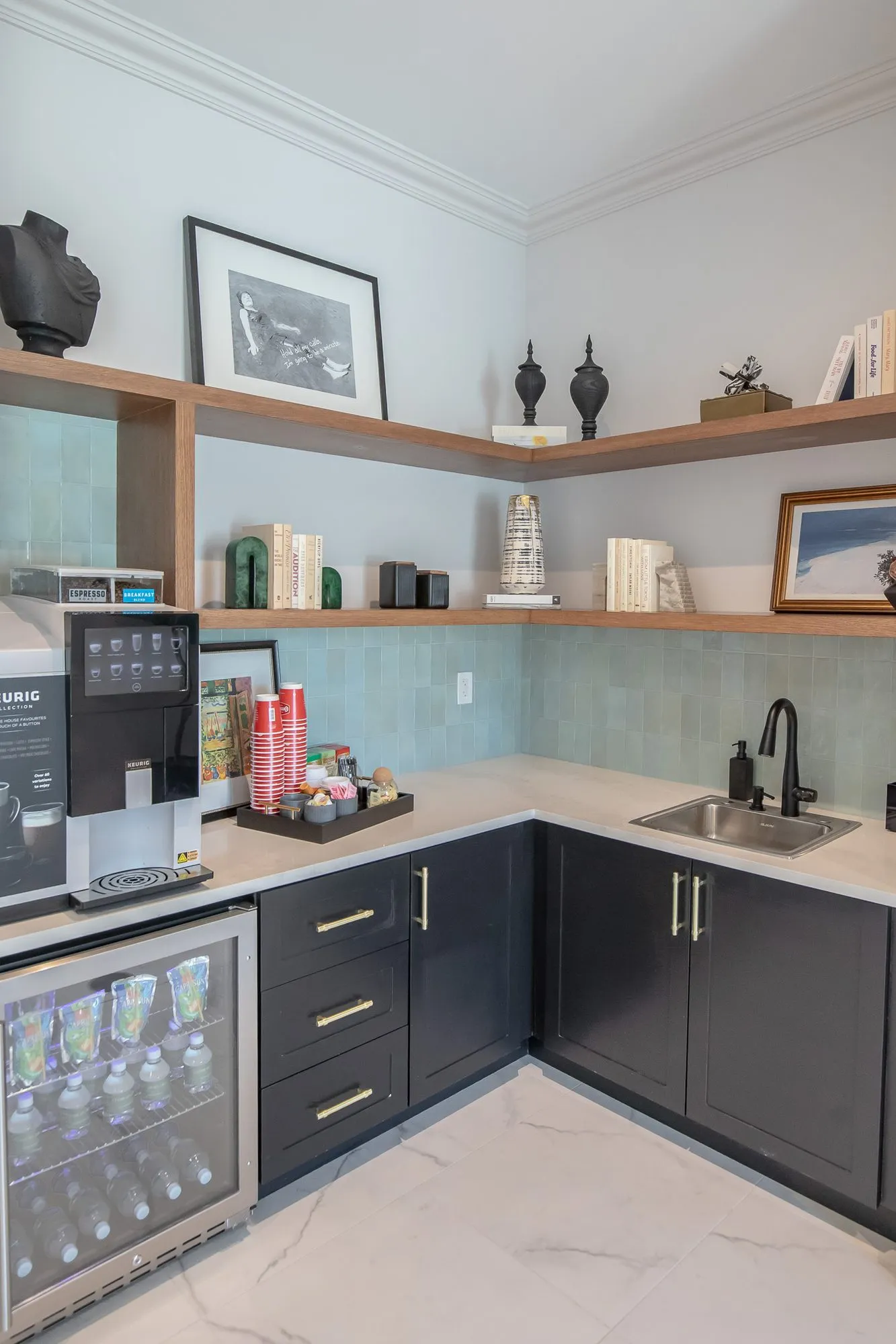Multifamily amenity coffee bar with black lower cabinets, a beverage fridge, sage tile backsplash and open wood shelves