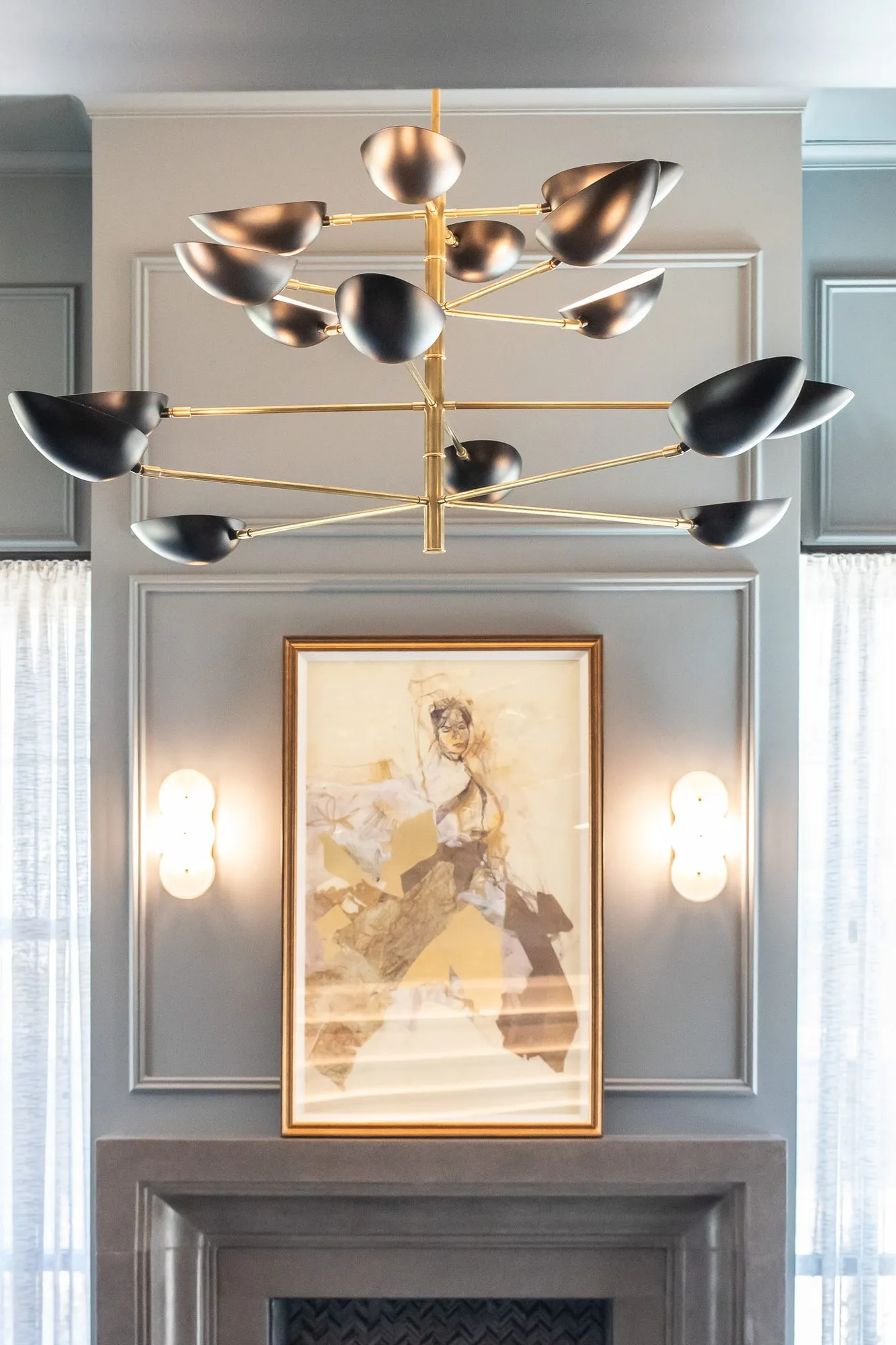 Multifamily amenity sitting room with a brass bird chandelier above a gilt-framed figure collage over the fireplace
