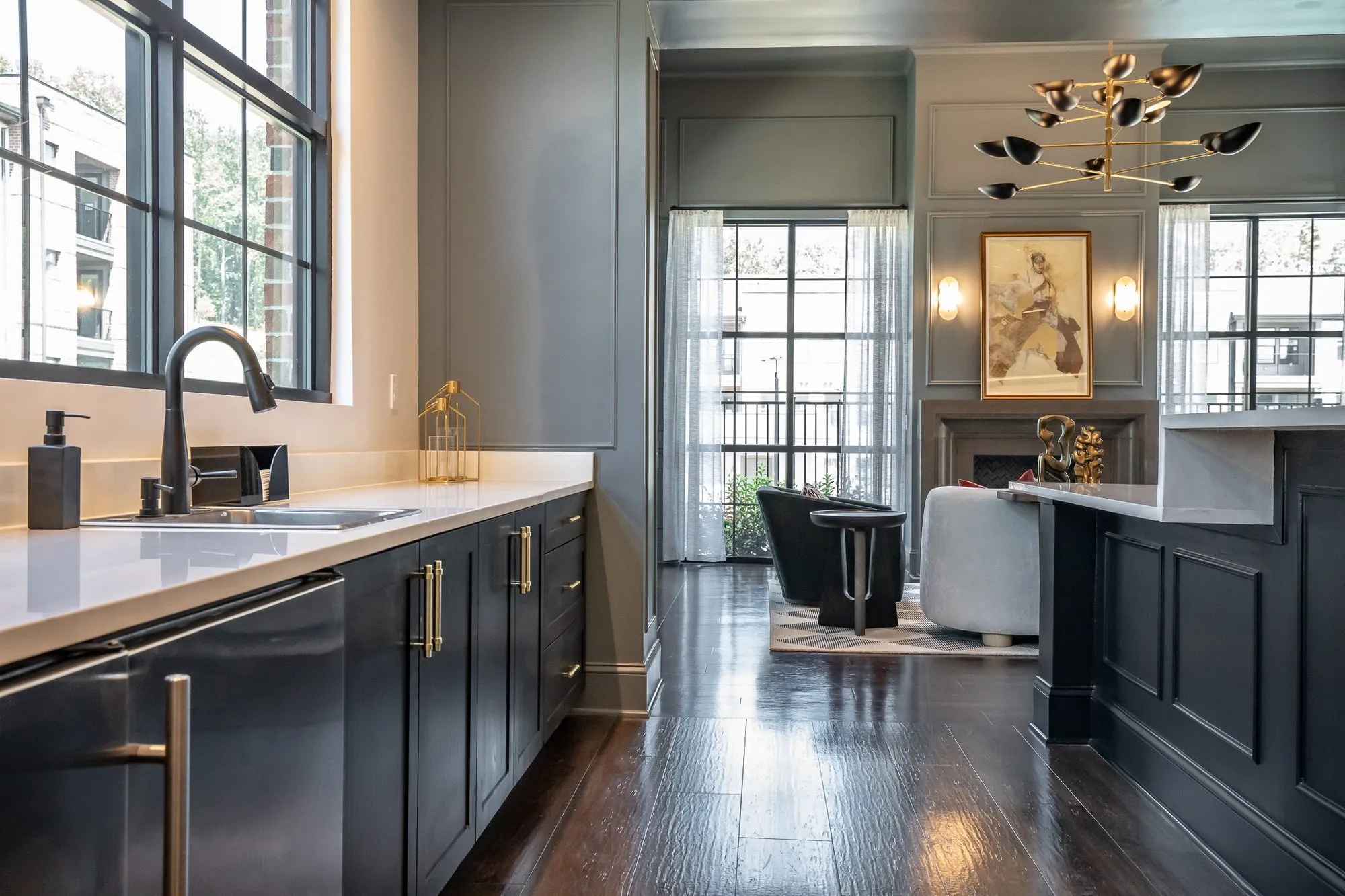 Multifamily amenity dark kitchenette with a white counter and black faucet, the grey panelled lounge and fireplace beyond