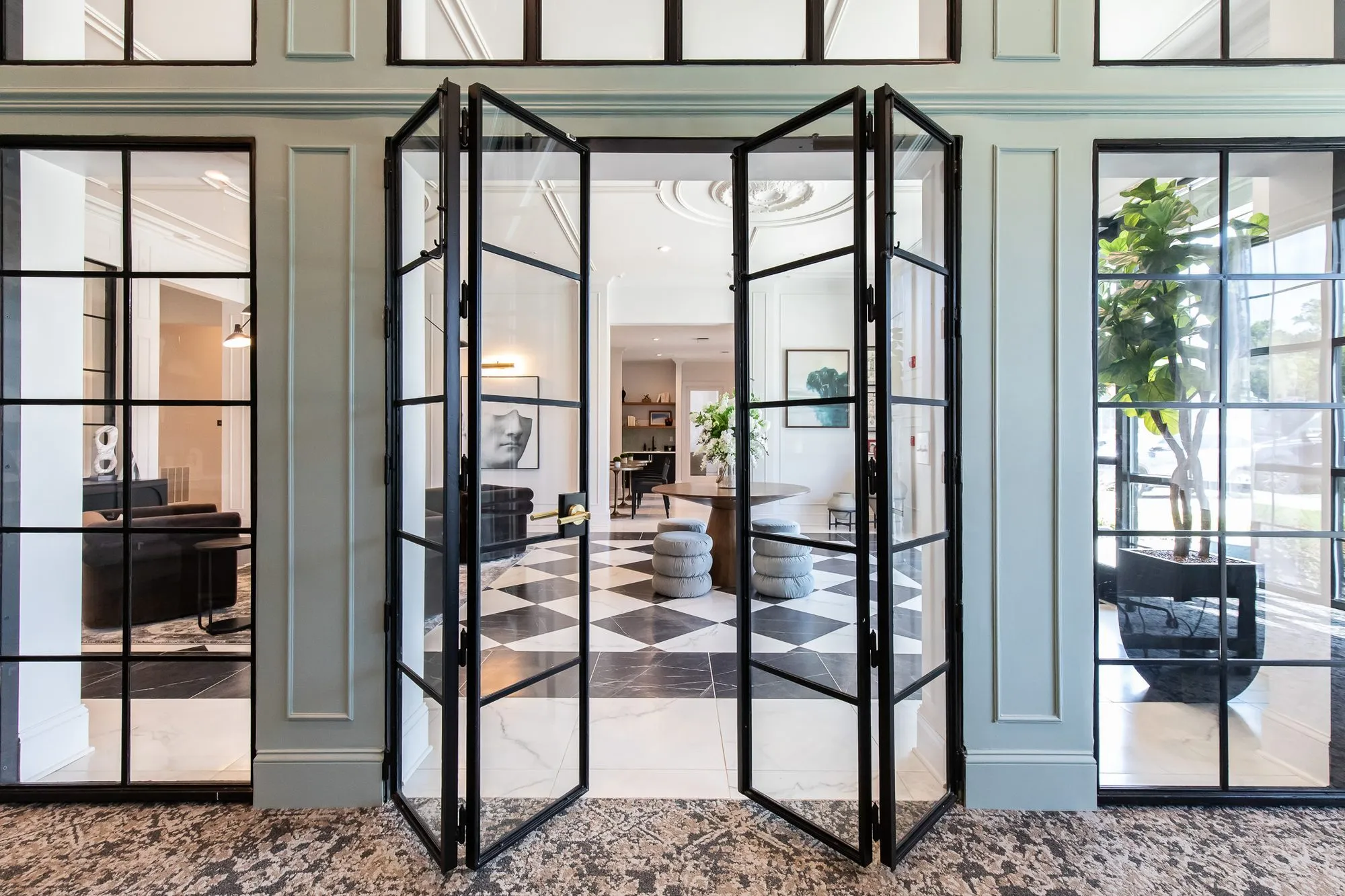 Multifamily amenity leasing office with black steel French doors open from the sage panelled room onto the checkerboard lobby