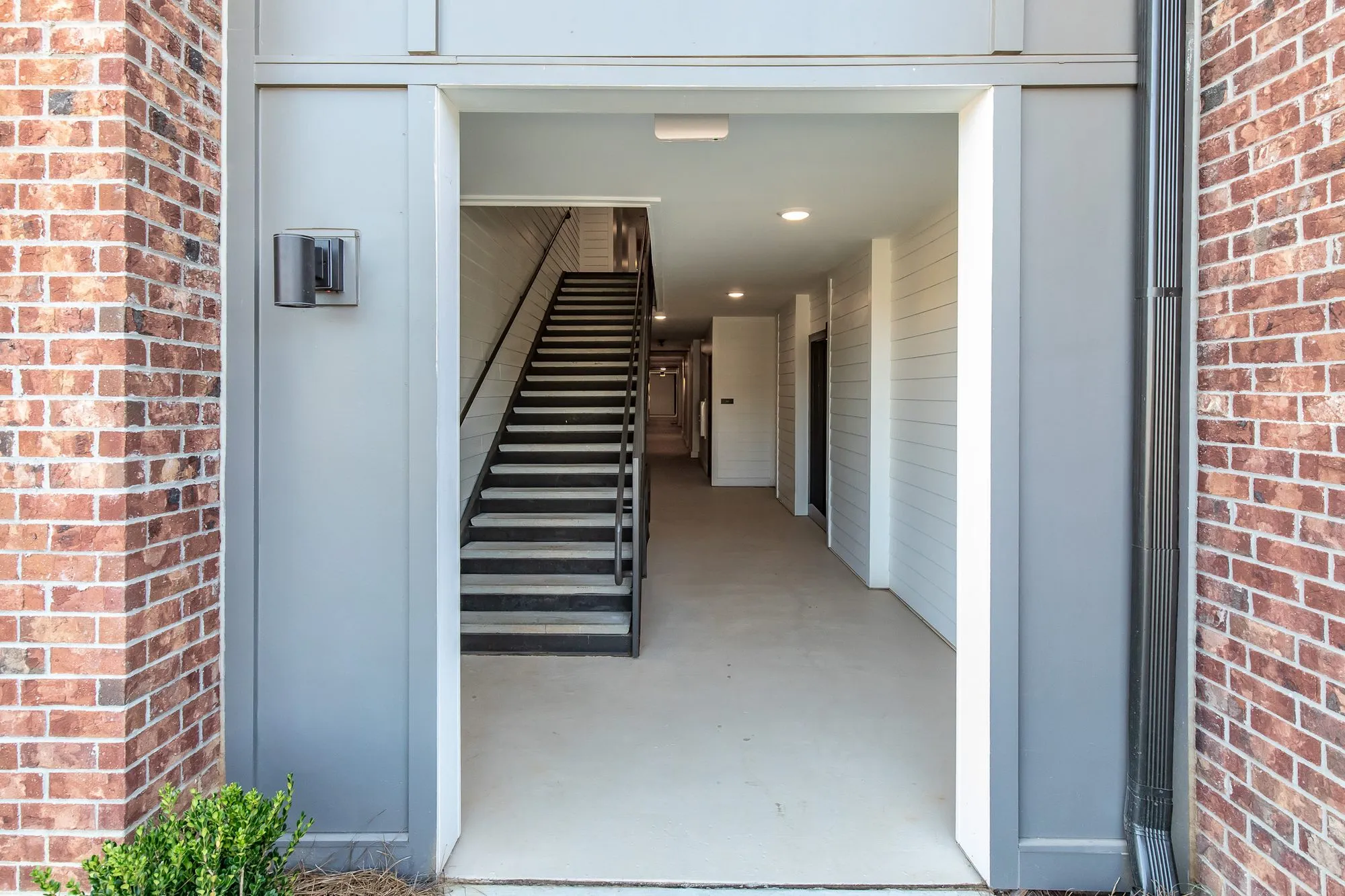 Multifamily community breezeway through a brick building with grey trim, a stair along the white shiplap corridor beyond