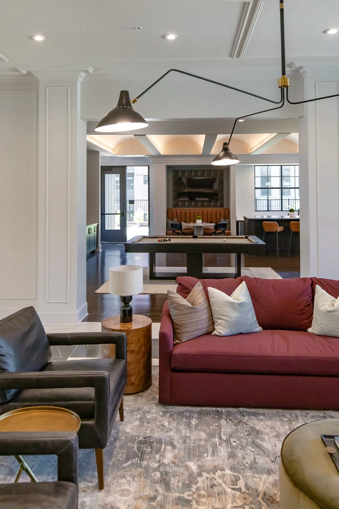 Multifamily amenity clubroom seen past a black leather armchair to a burgundy sofa, the billiards table and bar beyond