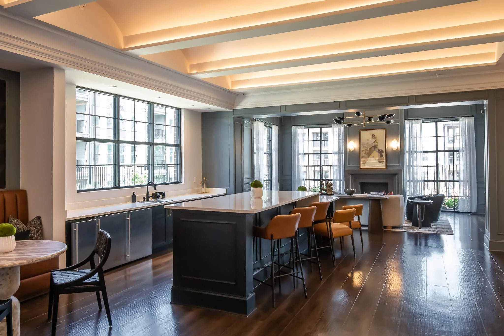 Multifamily amenity clubroom bar with orange leather stools along a dark island under a coffered ceiling, fireplace beyond